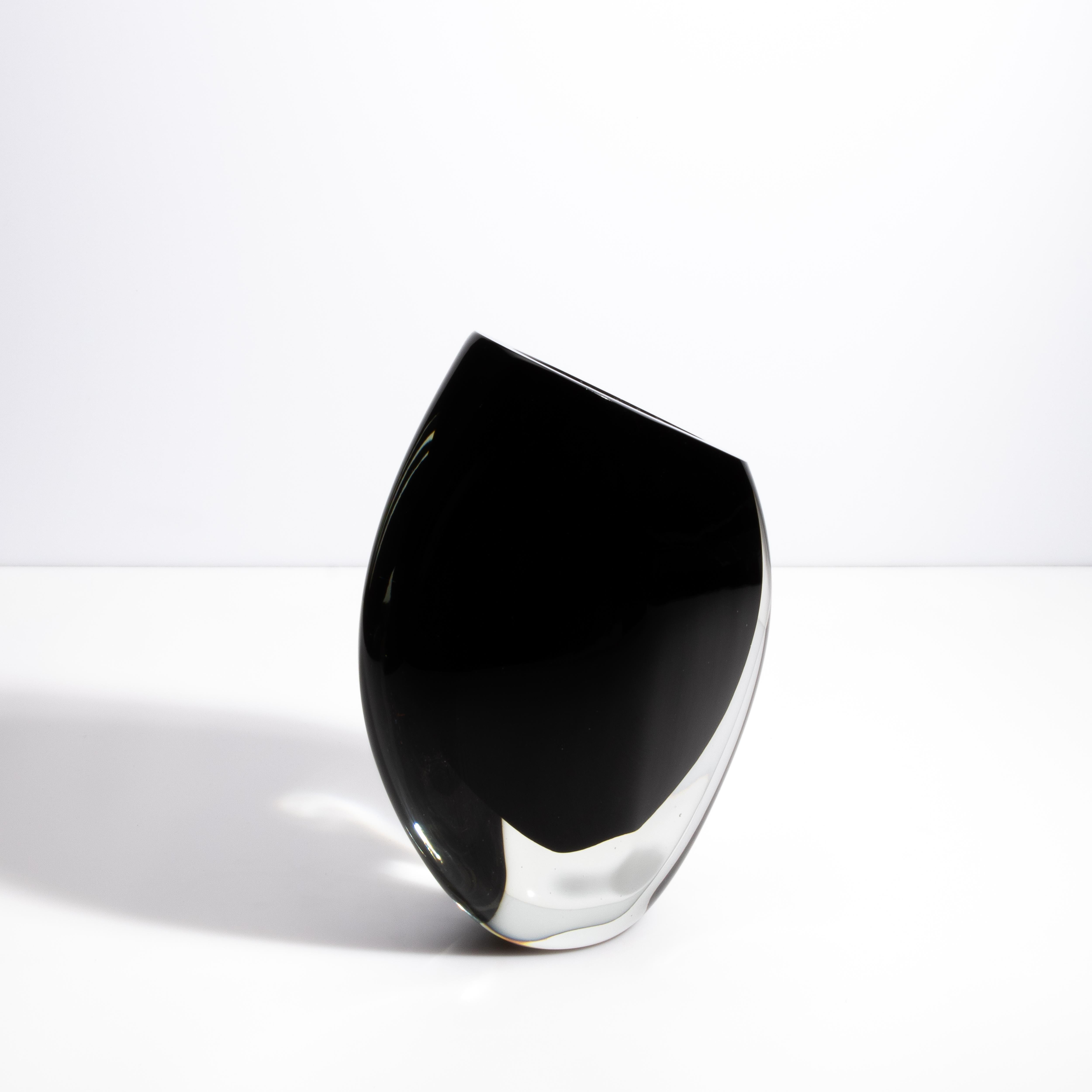 Questo elegante vaso in vetro di Murano incarna la raffinatezza e l'arte senza tempo dei vetrai veneziani. La sua tonalità nera profonda, in contrasto con i bordi in vetro cristallino, evoca un senso di lusso moderno. La silhouette elegante e