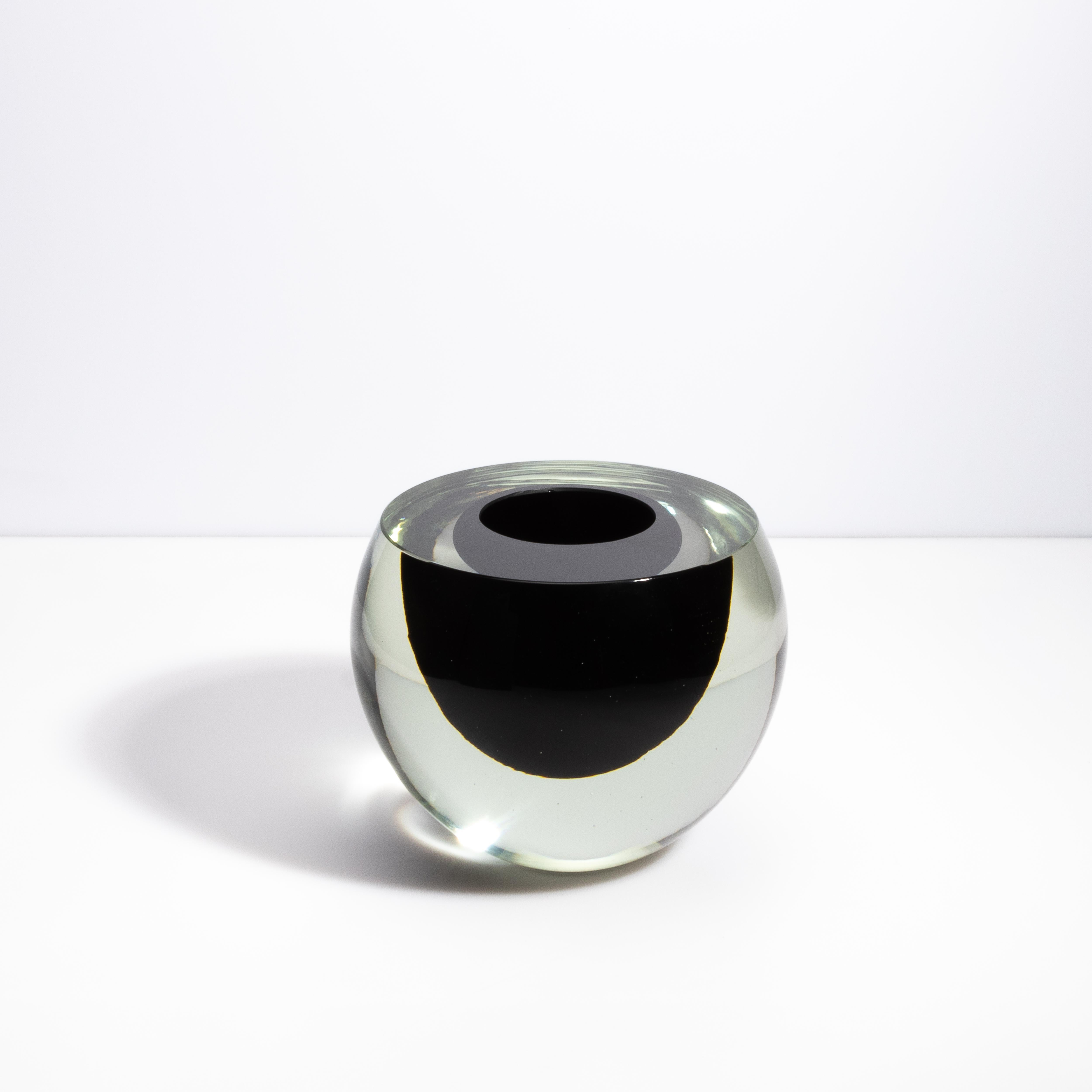 Questo vaso di Murano soffiato a mano, con la sua elegante forma sferica, è un pezzo notevole che incarna l'arte senza tempo della lavorazione del vetro di Venezia. Il vaso è caratterizzato da un'accattivante combinazione di vetro trasparente e nero