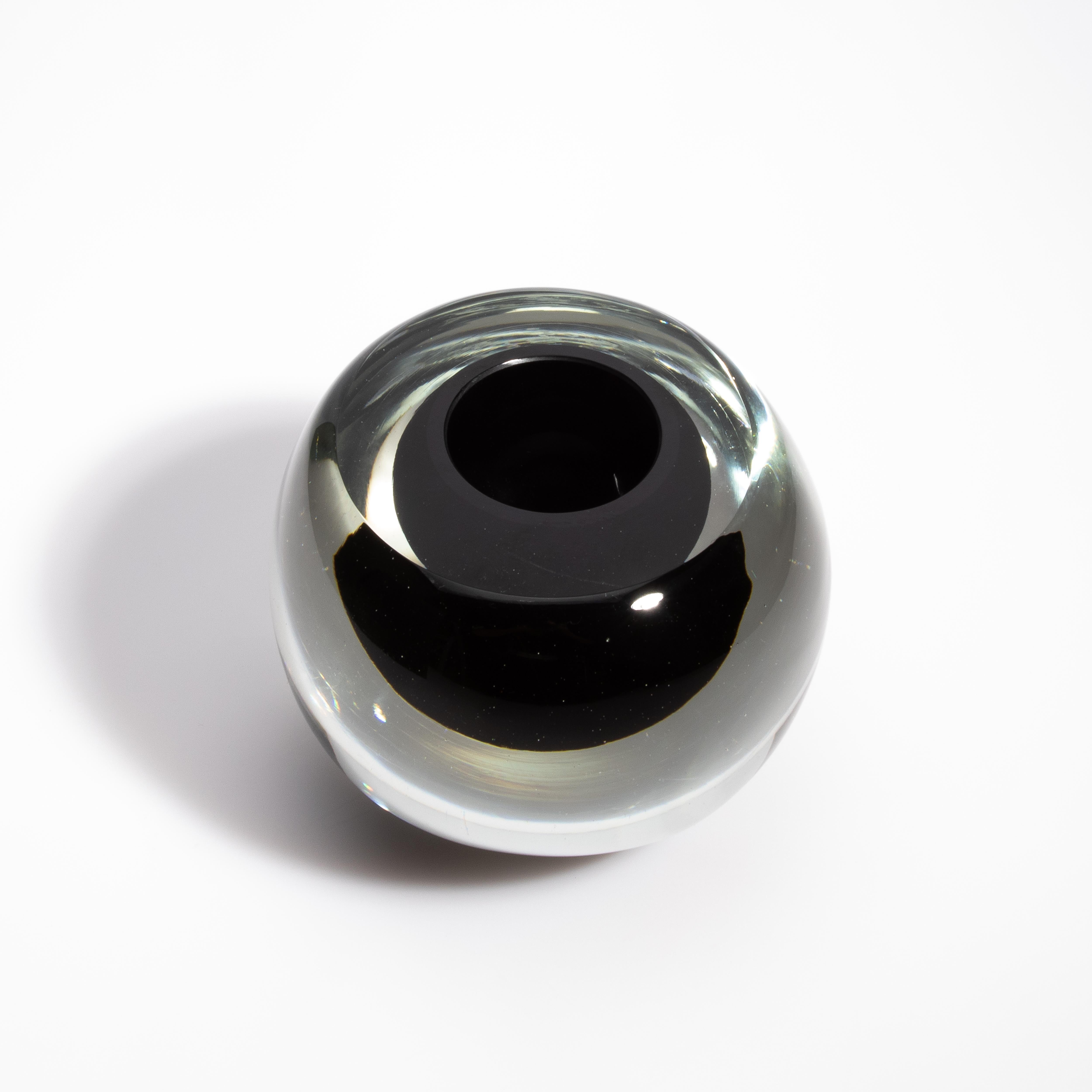 Questo vaso di Murano soffiato a mano, con la sua elegante forma sferica, è un pezzo notevole che incarna l'arte senza tempo della lavorazione del vetro di Venezia. Il vaso è caratterizzato da un'accattivante combinazione di vetro trasparente e nero
