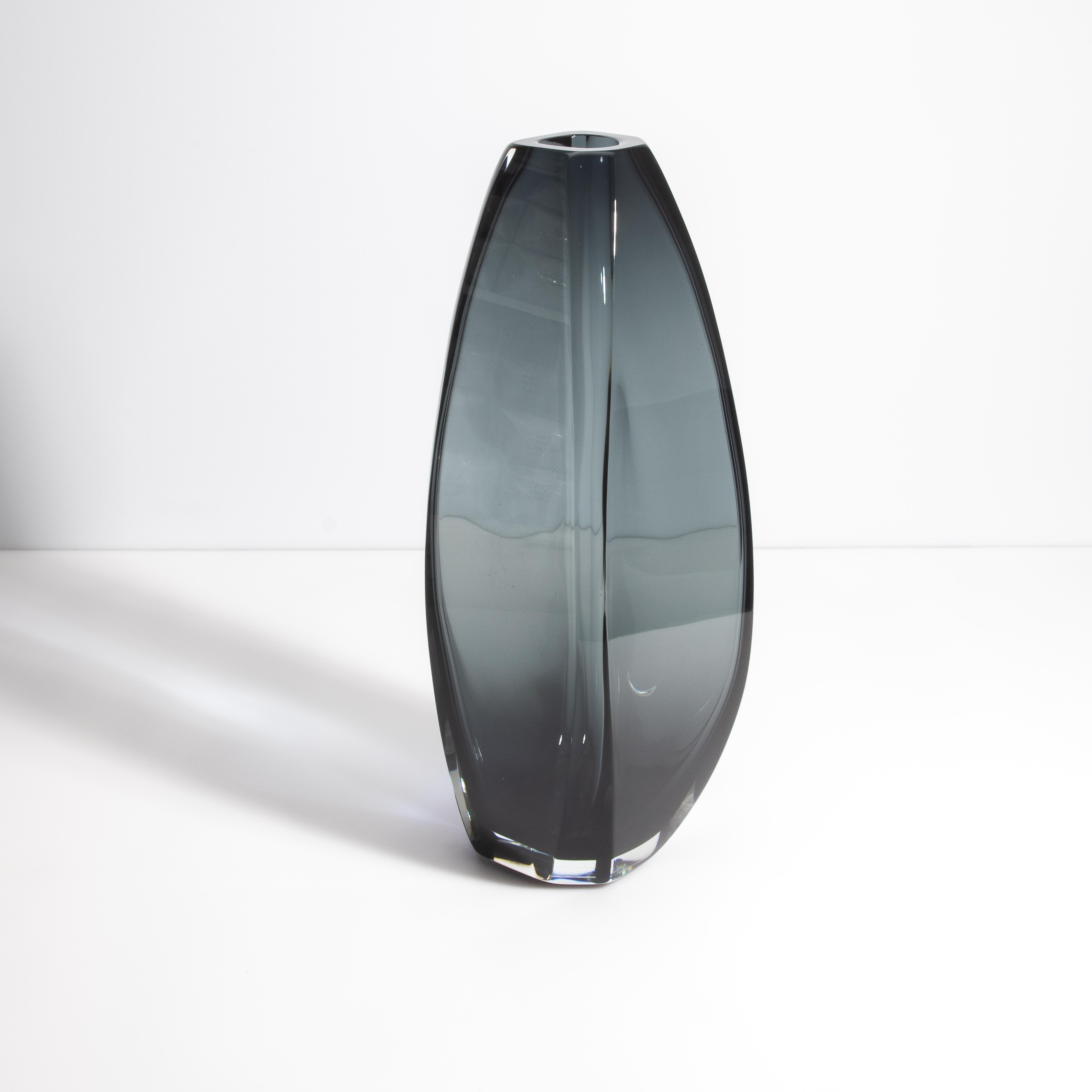 Sehen Sie sich die Eleganz unserer extra hohen Murano-Vase an, eine faszinierende Verschmelzung von schlichtem Design und meisterhafter Handwerkskunst. Dieses exquisite Stück mit seinem ruhigen rauchgrauen Farbton ist ein Beweis für die Raffinesse