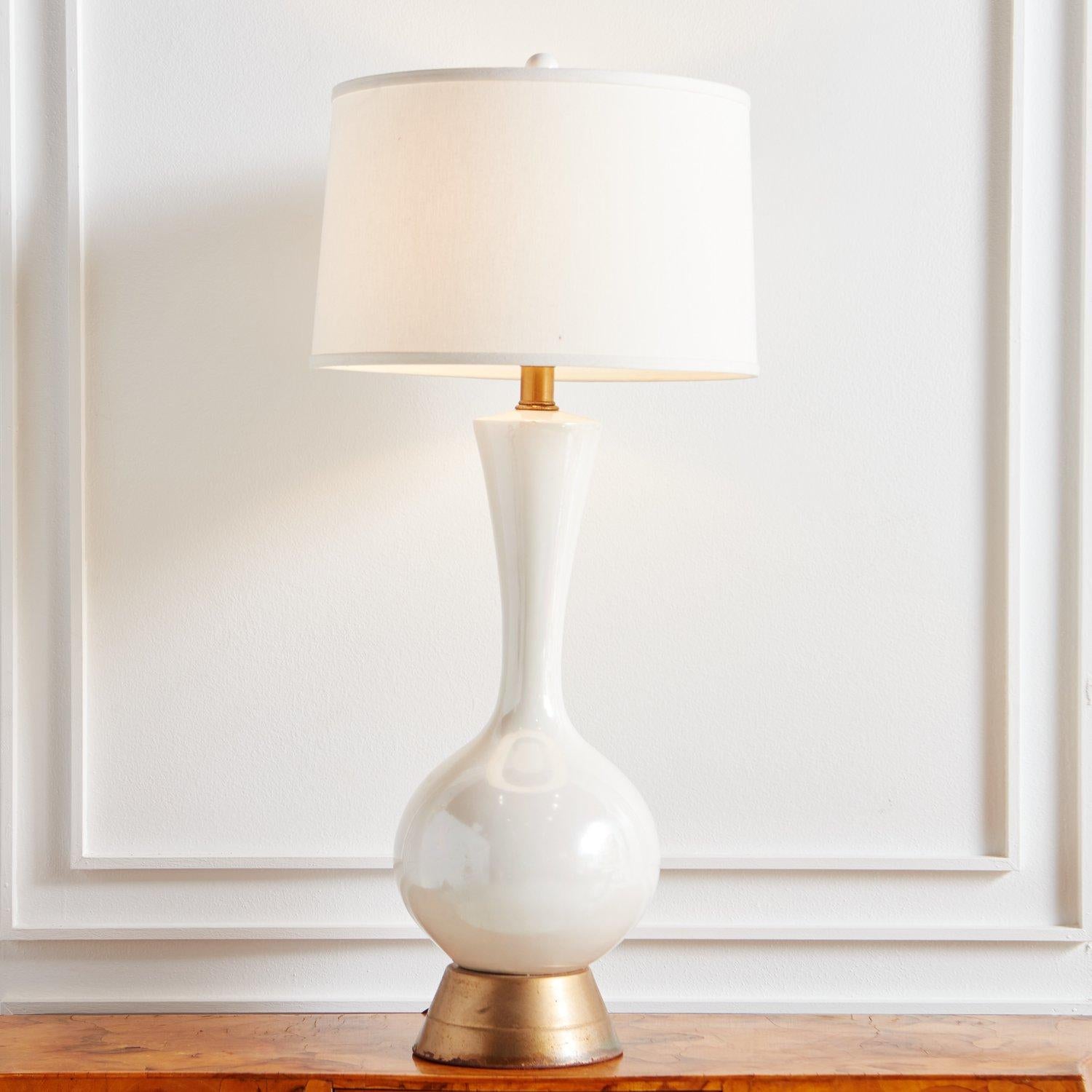 A tall, handblown glass table lamp featuring a curved body in a stunning opalescent hue. It has a tapered, circular brass pedestal base.