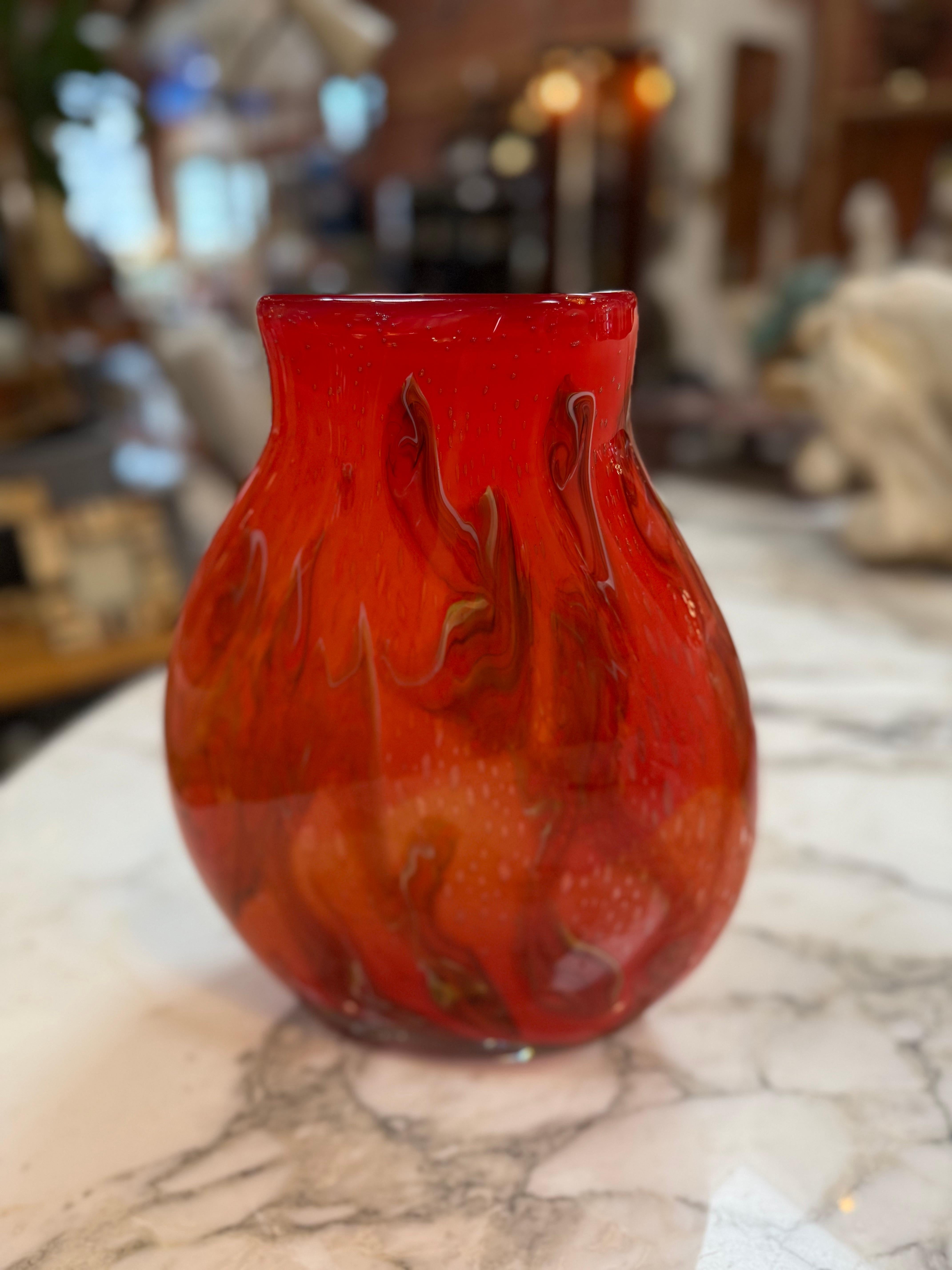 Vase en verre d'art Murano soufflé à la main, présentant un motif tourbillonnant rouge vif et orange. La pièce a un corps arrondi et bulbeux qui se rétrécit légèrement au niveau du col avant de s'évaser légèrement vers l'extérieur au niveau du bord.