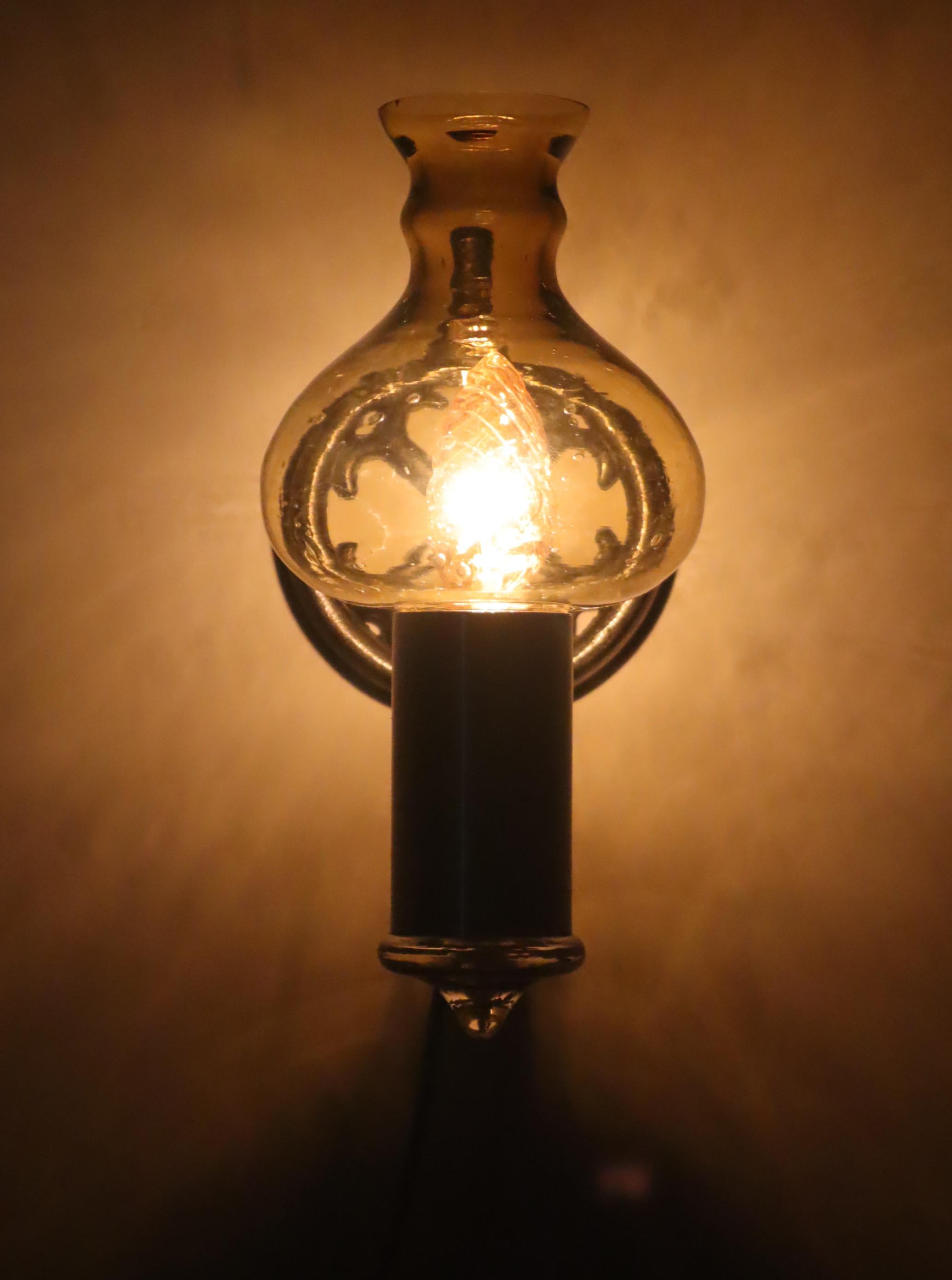 Il s'agit d'une lampe murale exceptionnelle fabriquée dans les années 1960. Elle possède un magnifique abat-jour en verre en forme d'oignon. Il s'agit d'une lampe suédoise. L'ampoule utilisée sur les photos la rend plus dorée ou jaunâtre, mais selon