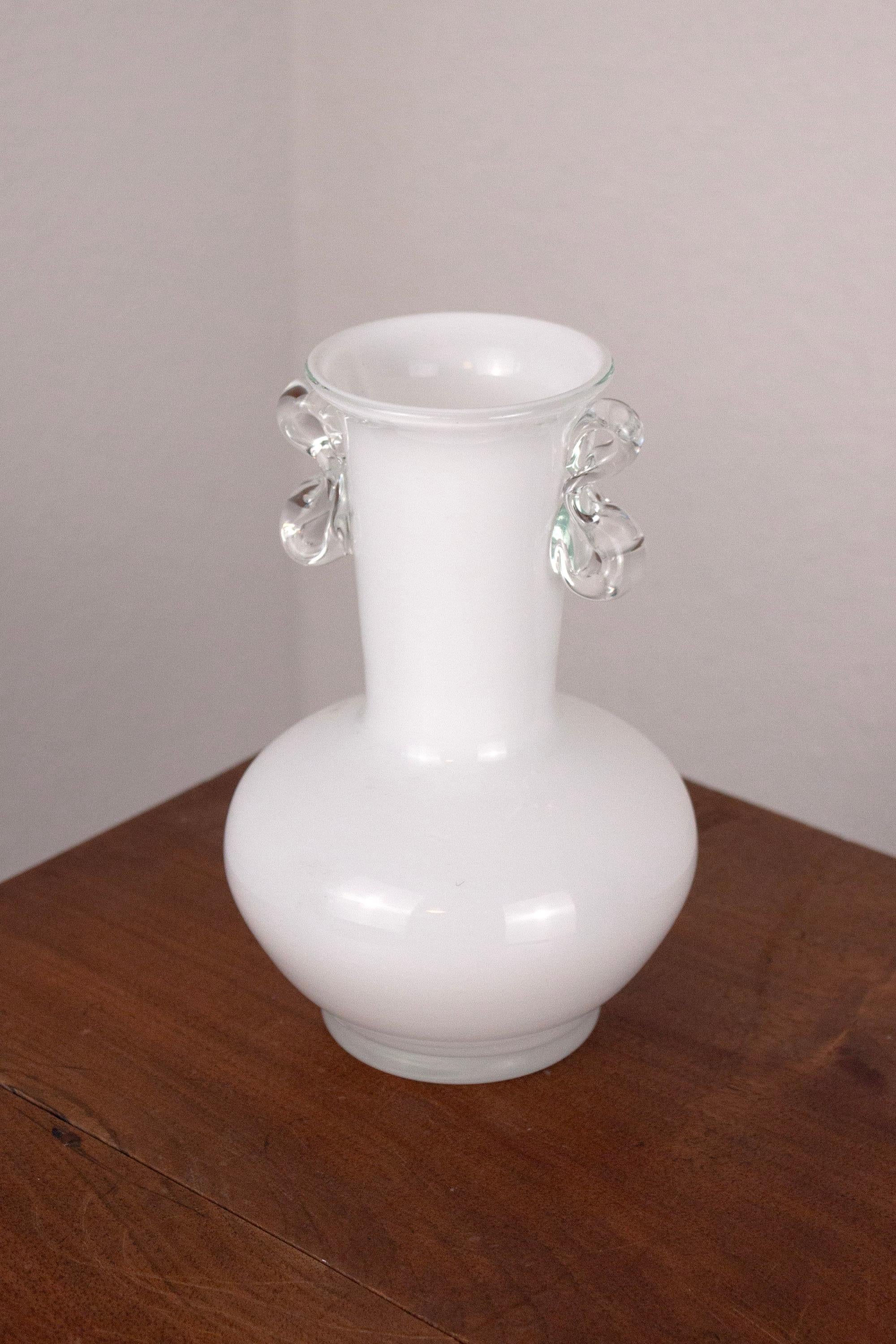 Cet élégant vase de style Amphora est fabriqué en verre clair et blanc soufflé à la main. Il présente une forme classique de balustre avec un bord évasé et deux poignées à volutes distinctives.

À la fois intemporel et polyvalent, ce vase sert à la