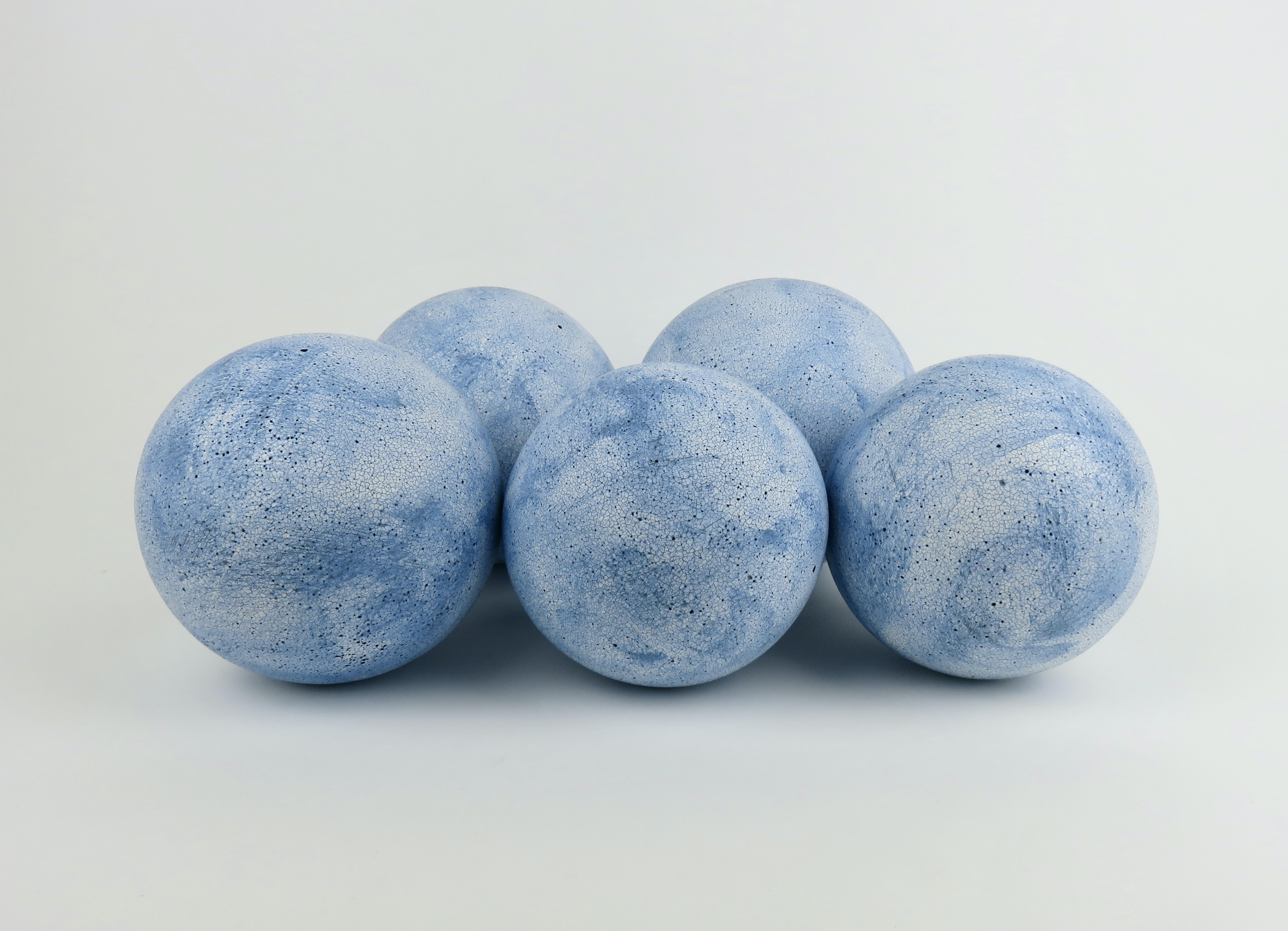 Cinq sphères bleu ciel, fabriquées à la main en grès céramique blanc. D'abord formé comme une sphère d'argile solide, puis évidé et rattaché. Après avoir beaucoup pataugé, gratté et rasé pour parfaire les formes, on les laisse sécher. Lorsqu'elles