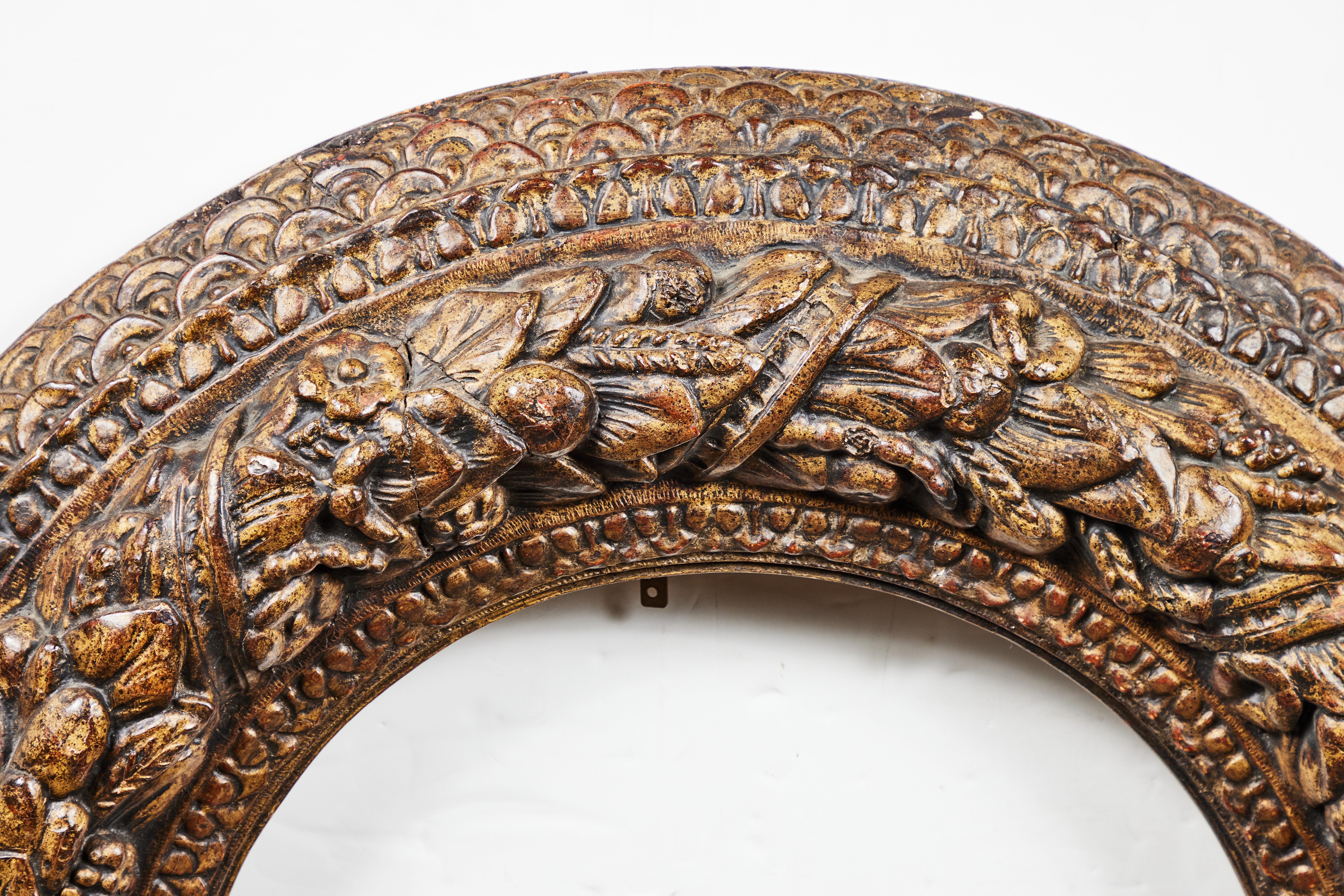 A striking, richly hand carved, gessoed, and gold gilded Italian roundel frame. The whole, intricately carved with a relief of a braided, floral and fruit garland bordered by stepped, fish-scale, and egg-and dart style patterns.