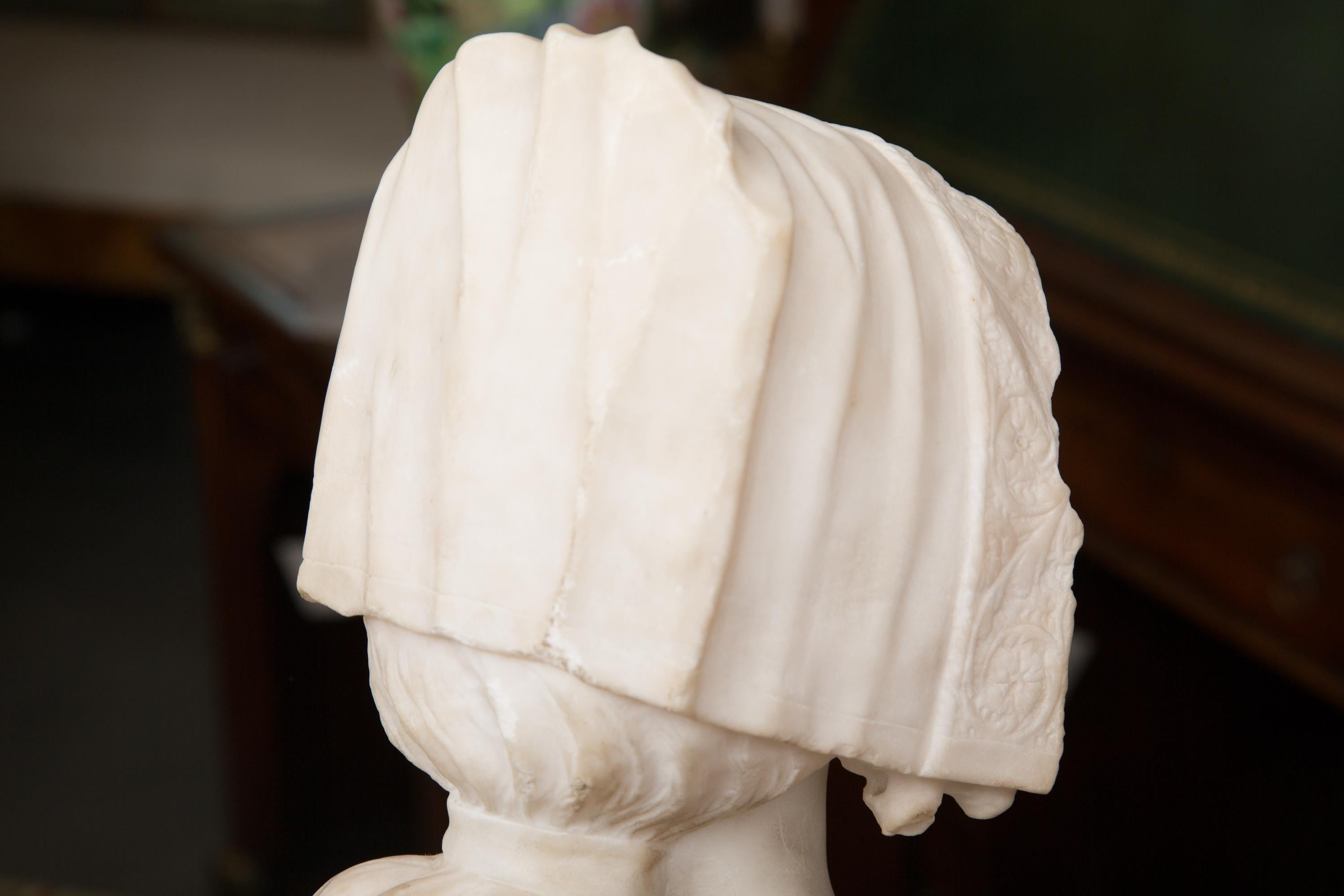 This is a delicate and gentle French Carrara marble sculpture of a young lady, wearing a lace head dress and cape. 19th century.