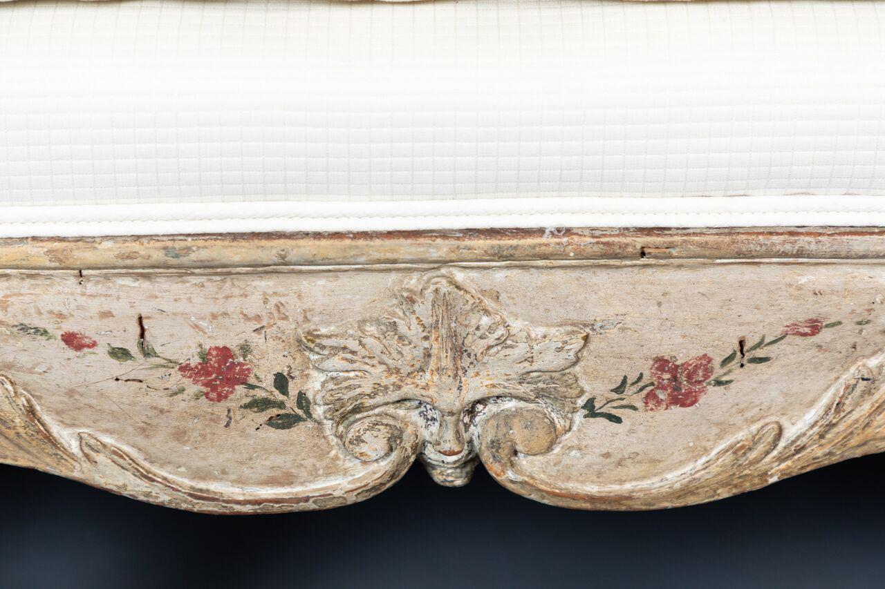 Beautifully carved and painted, serpentine Venetian sofa embellished with flowers throughout. The top-rail features a relief-carved vase overflowing with a tumble of blossoms. Upholstered in a contemporary, white, fabric.