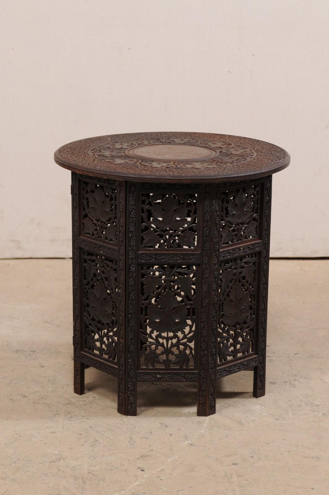 An Anglo-Indian hand carved side table with round top from the mid-20th century. This vintage table from India, with a round-shaped top measuring approximately 24