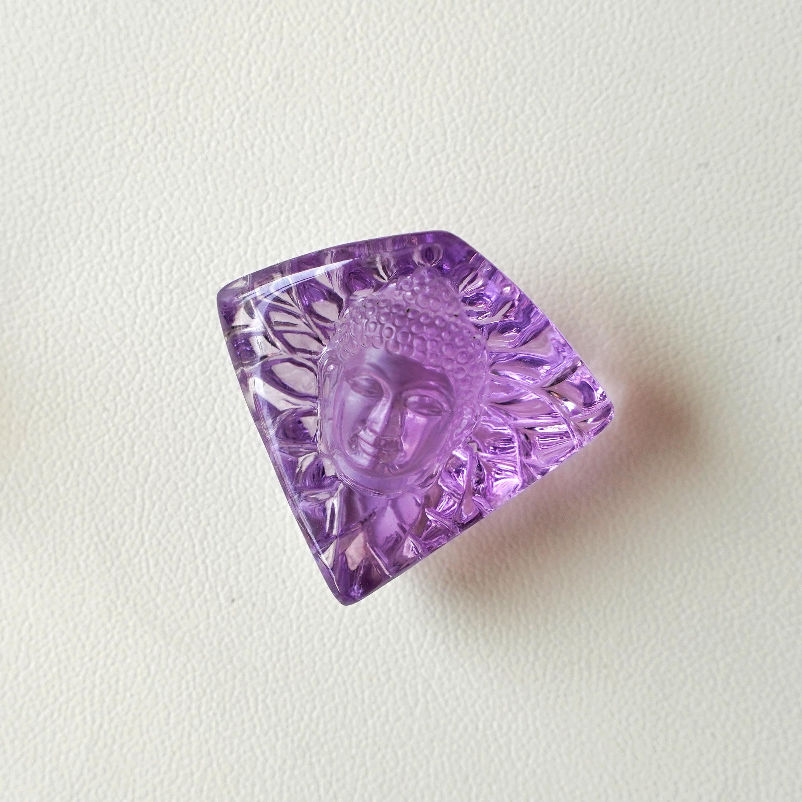 This buddha face carving on natural brazilian lavender amethyst is hand-carved with extreme detail by our expert lapidary artist in Jaipur which transform raw stones into unique art works. 
The gemstone is of very good quality with Lavender color