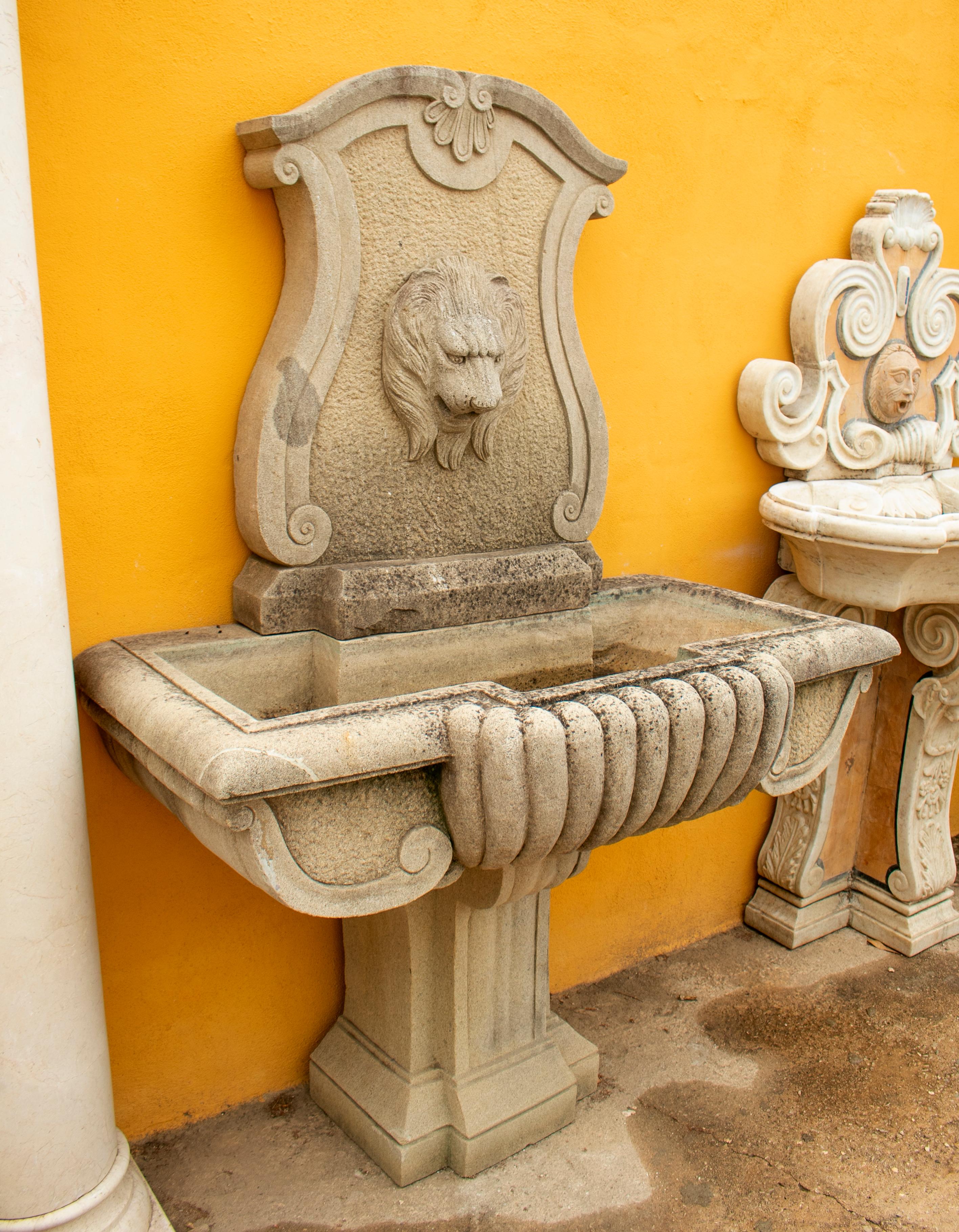 Hand carved aged stone wall fountain with lion head.