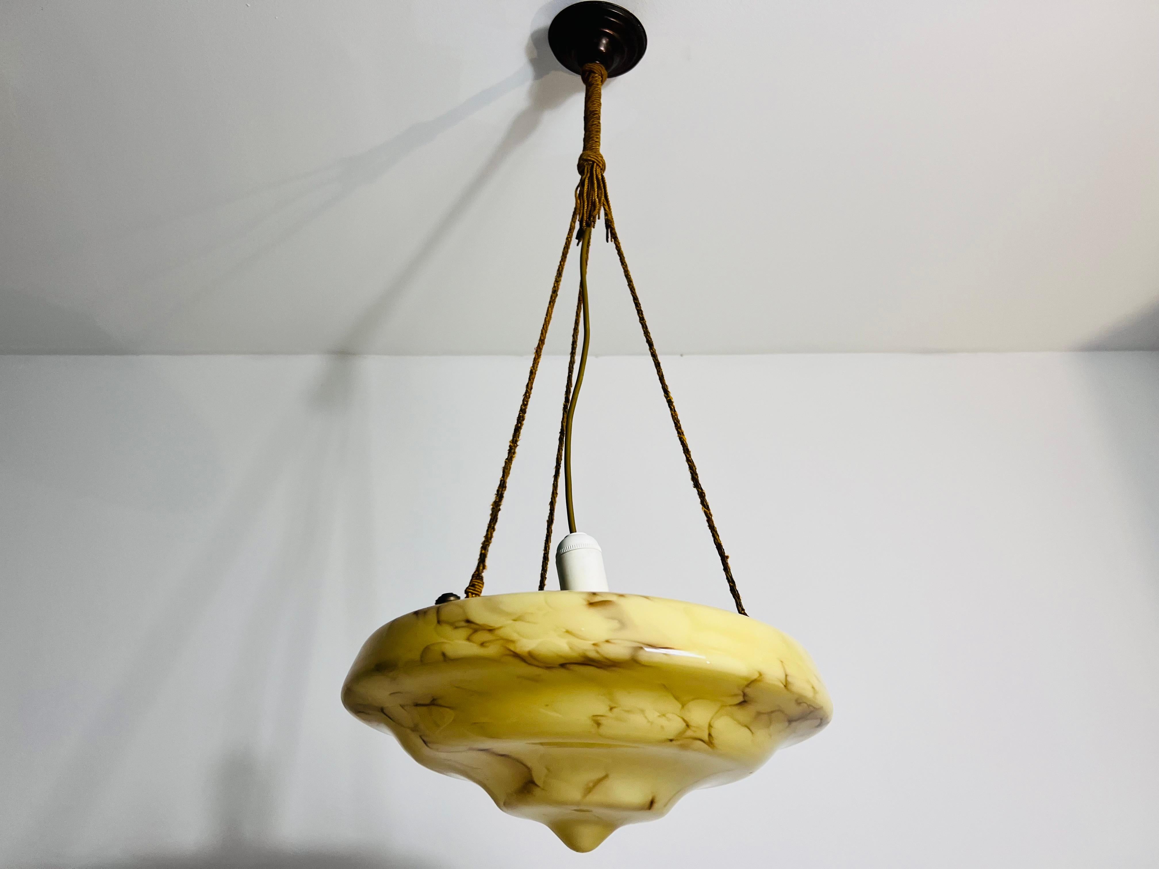 Bellissima lampada a sospensione in vetro degli anni '30, realizzata in Germania. La luce morbida e diffusa che passa attraverso il vetro venato crea un'atmosfera calda e invitante, rendendolo un perfetto centrotavola per qualsiasi stanza. Il suo