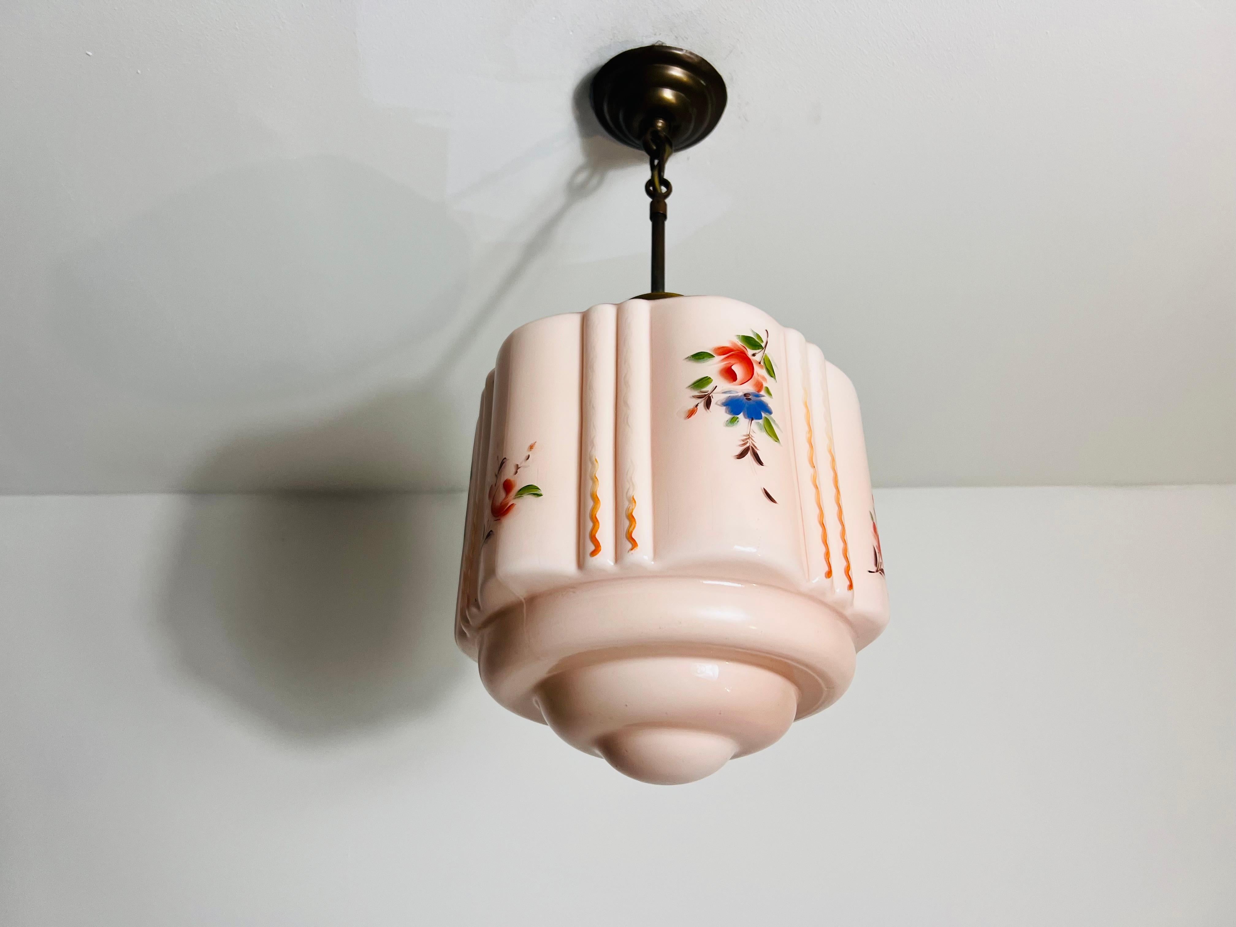 This exquisite ceiling lamp from 1930s Germany exudes timeless elegance and charm. The lampshade is crafted from genuine pink glass, featuring delicate floral motifs that add a touch of sophistication. The lamp is suspended by a sturdy brass chain,