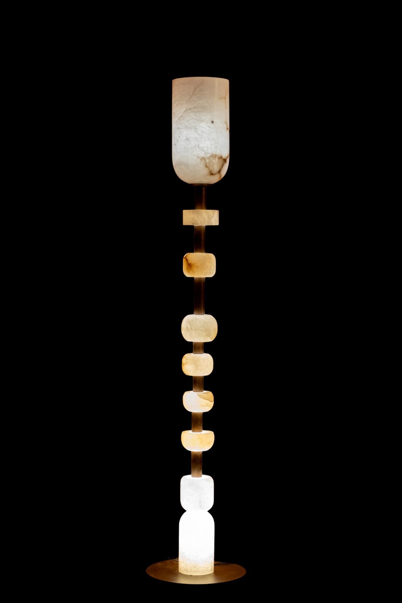 The Tottem Floor Lamp is a tall, sculptural light that looks like a modern piece of art. It is made by stacking smooth alabaster stone blocks on a strong metal base. When the lamp is switched on, the natural stone gives off a soft, warm glow that