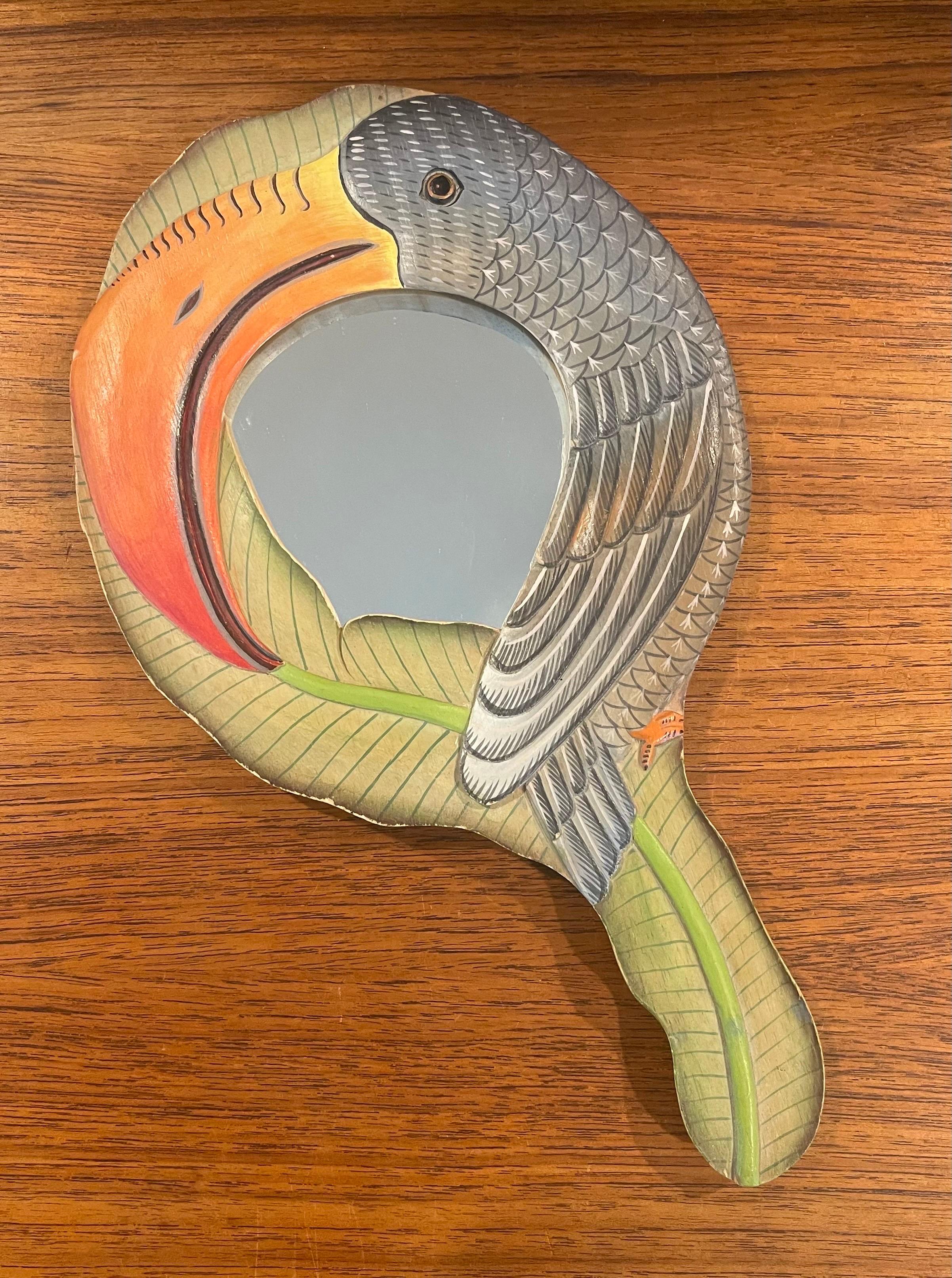 A nice hand carved and painted toucan hand mirror, circa 1980s. The mirror is beautifully hand crafted and brightly colored with a toucan and its beak encircling the hand mirror. The piece is in very good condition and measures 7.375
