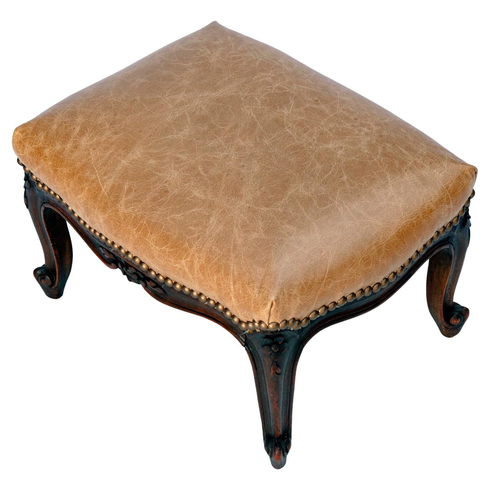 Hand carved Antique French Leather Footstool19 Hand carved Antique French Antique leather footstool delicately hand carved antique French footstool newly upholstered in a fine aniline dyed leather with decorative brass nailheads. See less
