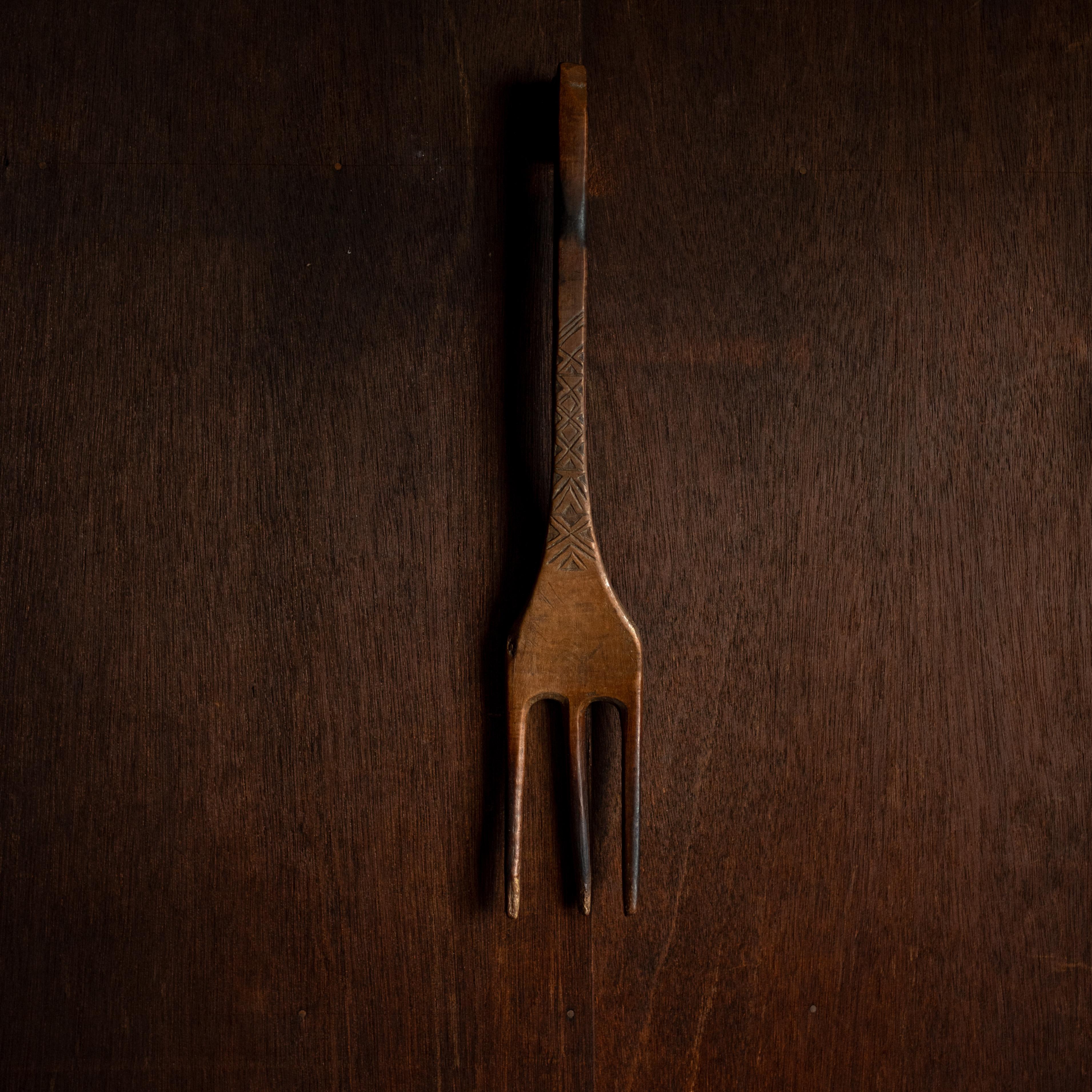 Un expresivo y escultural tenedor antiguo de madera tallada. Este utensilio de tres puntas presenta un cuello alargado y motivos geométricos grabados a mano a lo largo del mango, lo que sugiere un valor tanto funcional como decorativo.

Esta pieza