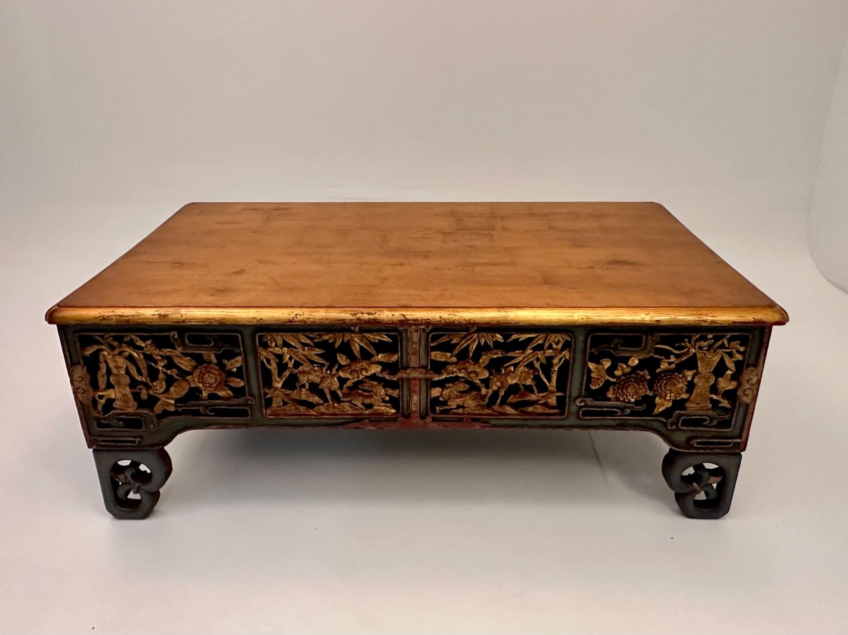 Glamorous beautifully crafted hand carved rectangular coffee table having meticulously detailed apron with birds and foliage and polychromed gilded red and green finish.  The top is a warm burnished gold.