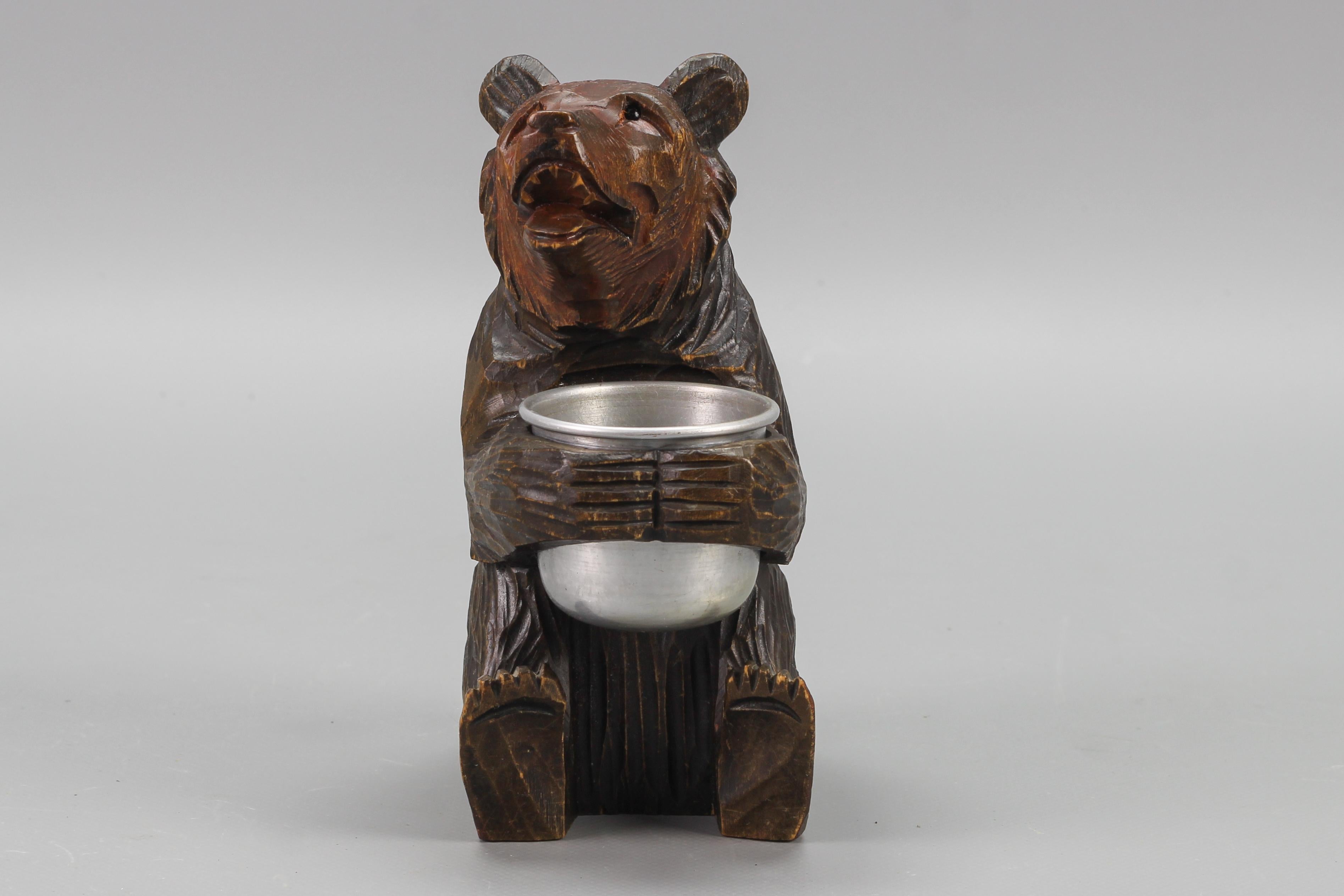 Hand-carved Black Forest style bear with aluminum pot, from ca. the 1920s.
This beautiful hand-carved wooden, linden-wood, seated bear is holding an aluminum pot. Nicely detailed, with glass eyes.
Can be used for the storage of small items on a