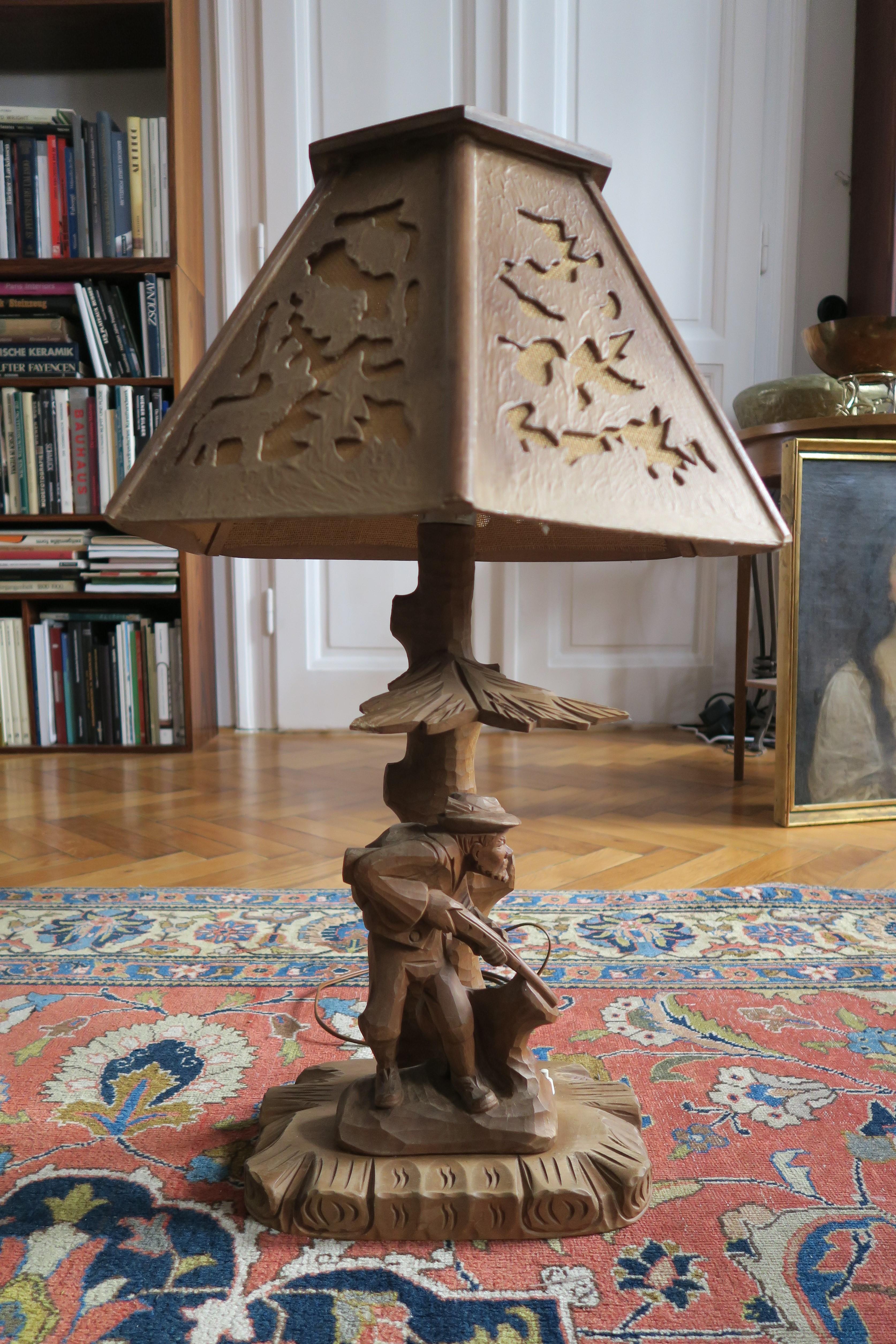 The item for sale is an original desk lamp in the style of Black Forest or possibly Swiss artisanal craftsmanship. Foot and lampshade are both hand carved from medium-dark wood. The lampshade also sports some abstract cutouts which were stretched