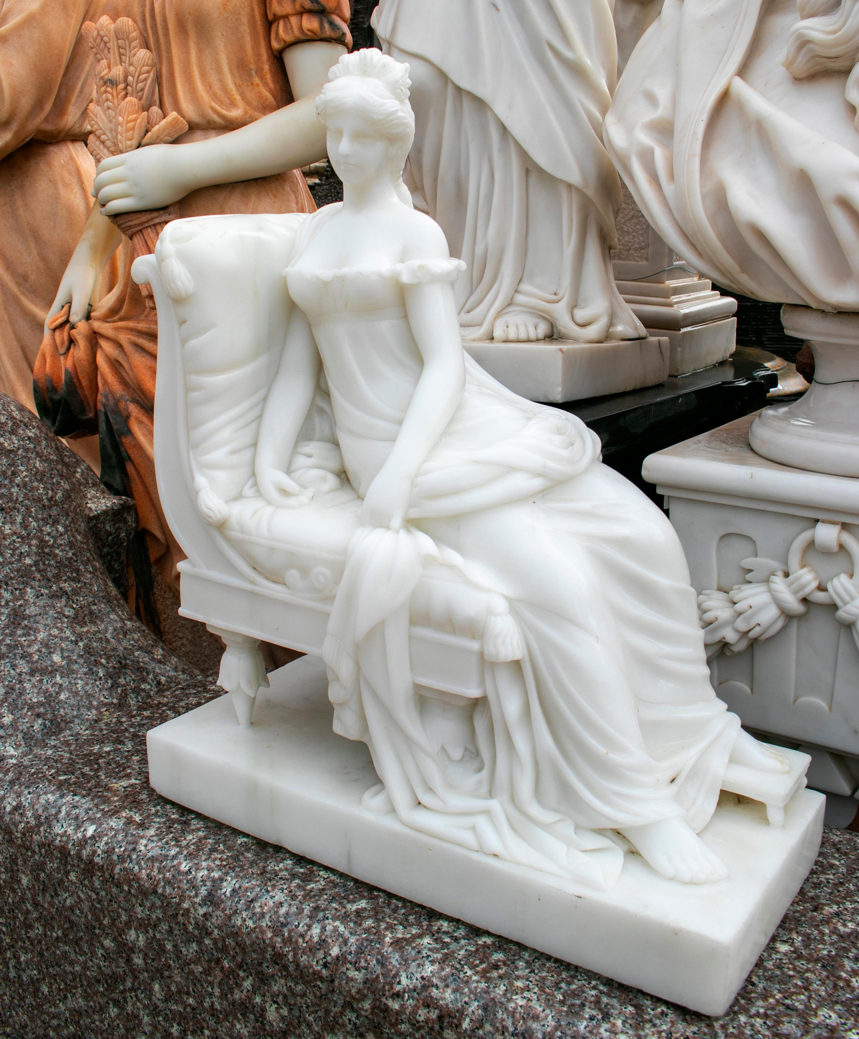 Hand carved classical white marble lady sitting on a chaise lounge.