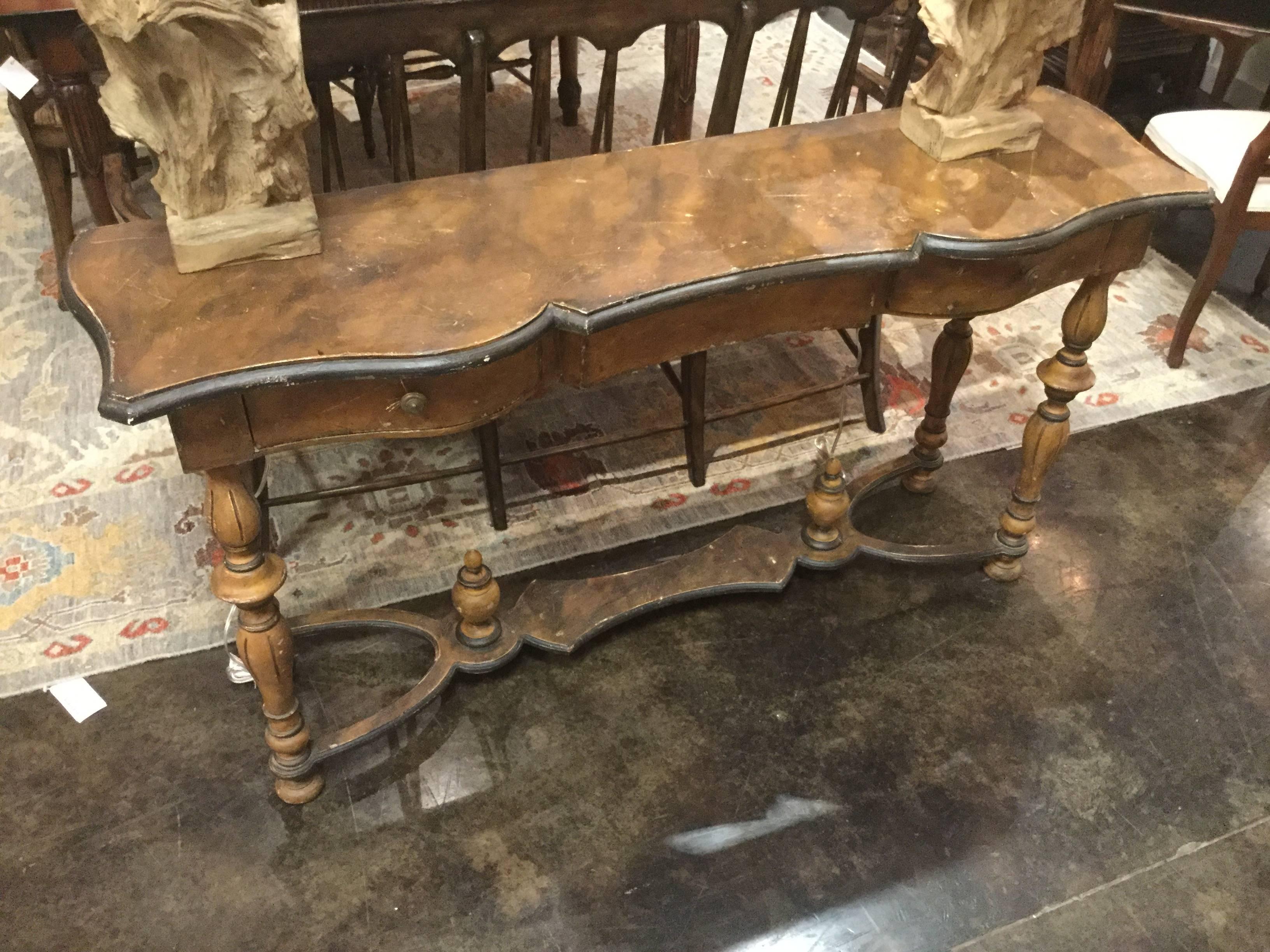 This rustic, hand-carved wooden console table has two drawers on the front, four decorated turned legs, and a X-stretcher for stability with two hand-carved finials. Hand-painted distressed antique finish. The piece is perfect for a living room,
