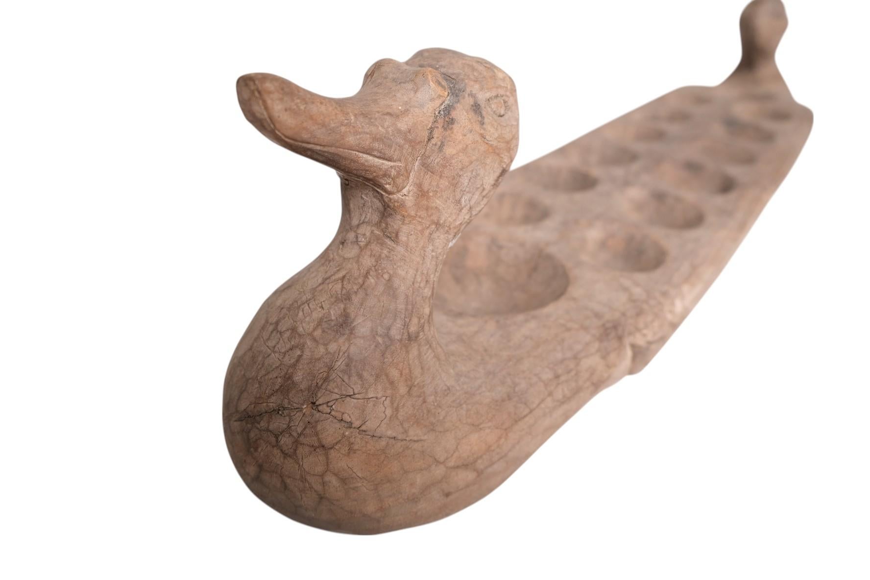 A beautifully hand-carved mancala board in the shape of a duck, likely originating from West Africa, mid-20th century. Crafted from a single piece of wood with rich patina and visible hand-tool marks, this folk art object features twelve carved game