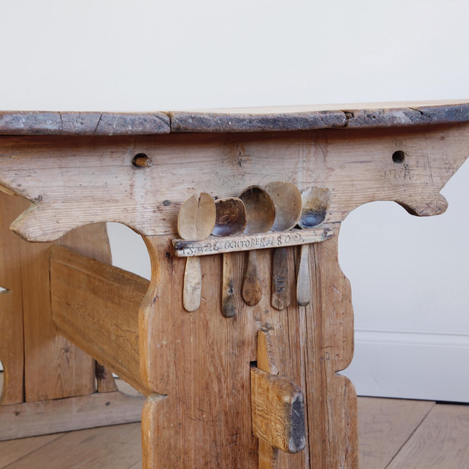 This hand carved pine trestle table is a wonderful example of Swedish folk furniture from the Gustavian era. Most remarkably, it includes a rack built to hold the wooden spoons of each family member, and the five spoons themselves. We have never