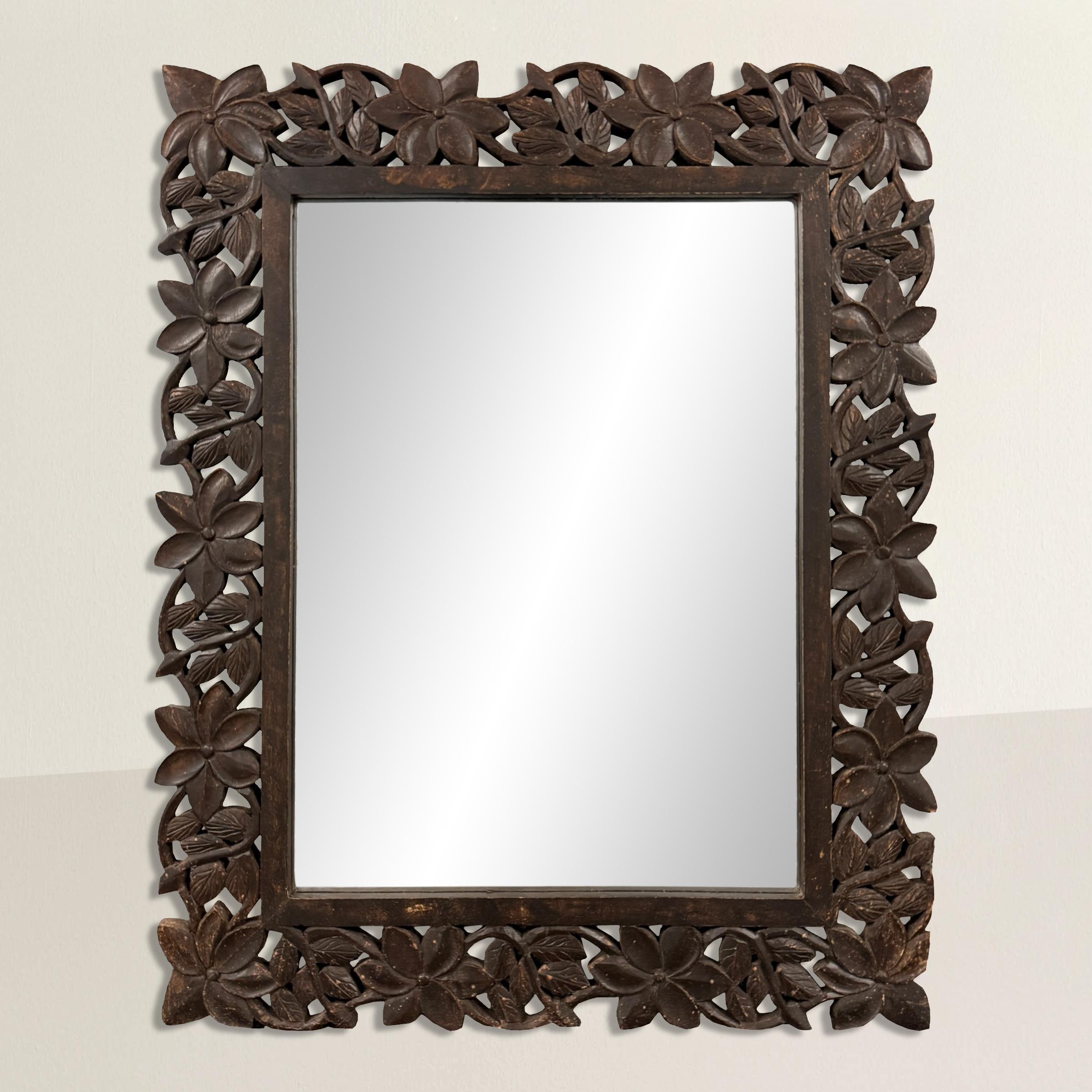 This 20th-century hand-carved wood framed mirror is a stunning blend of elegance and craftsmanship. The frame features a repeated floral and scrolling vine pattern, delicately carved to encircle the mirror, adding a touch of timeless beauty to any