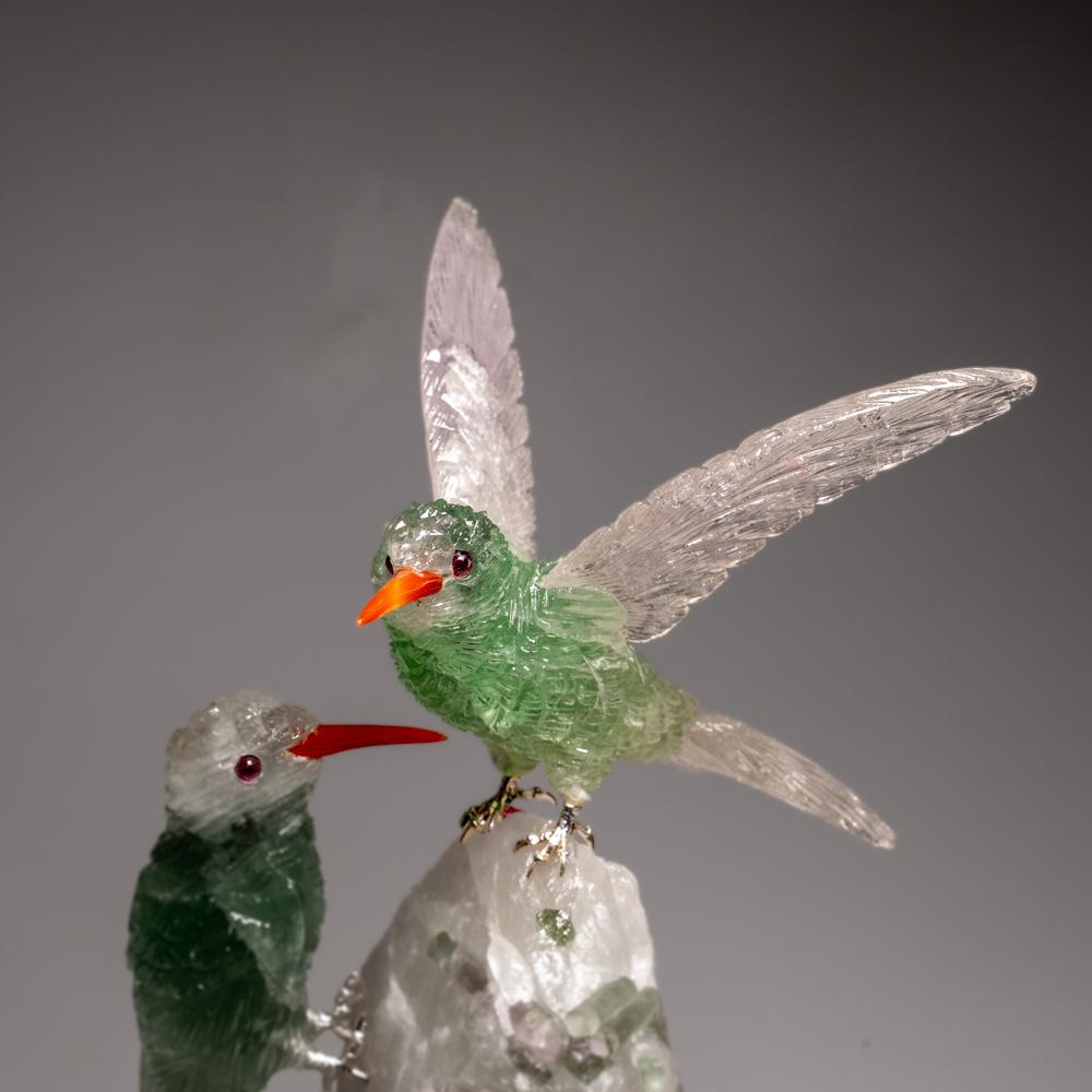 This Hummingbirds carving is a unique piece of art, carved from museum-quality fluorite with onyx eyes and a carnelian beak. The owls is perched atop a green tourmaline and quartz matrix and mounted on a custom stand for convenient display. This