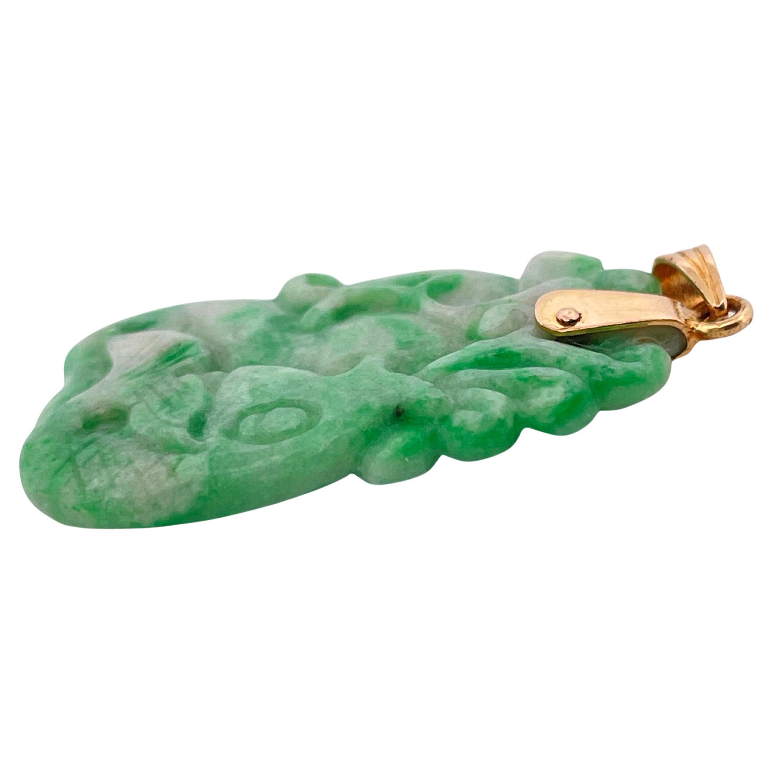 This elegant pendant showcases a beautifully hand-carved green jade centerpiece, celebrated for its rich, mottled hues ranging from deep emerald to soft celadon. The jade is intricately sculpted with flowing, organic patterns that highlight the