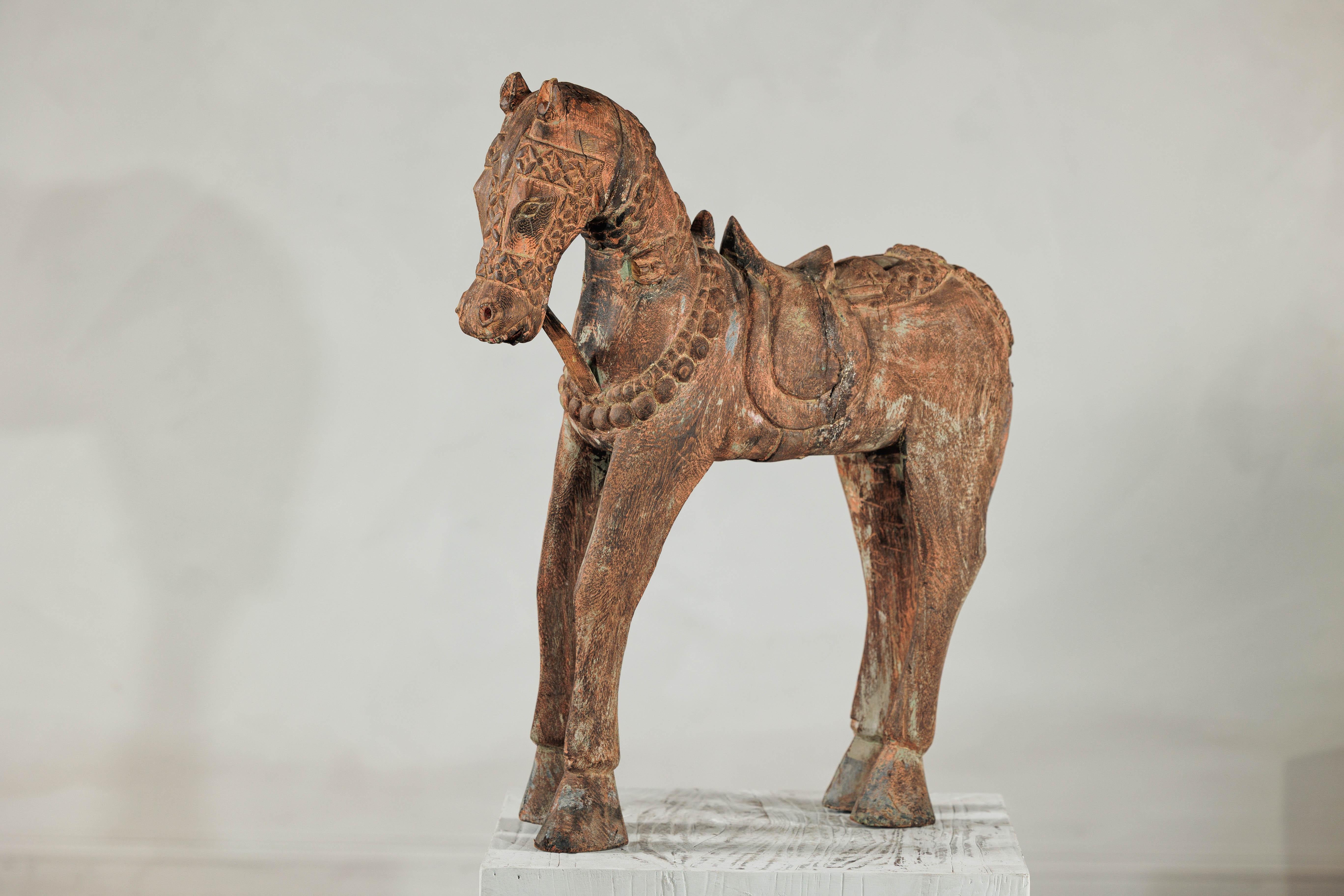 This rustic carved wooden horse captures the enduring elegance of traditional Indian craftsmanship. Hand-hewn from solid wood and painted in earthy tones with faint traces of original polychrome, the sculpture is richly textured with engraved