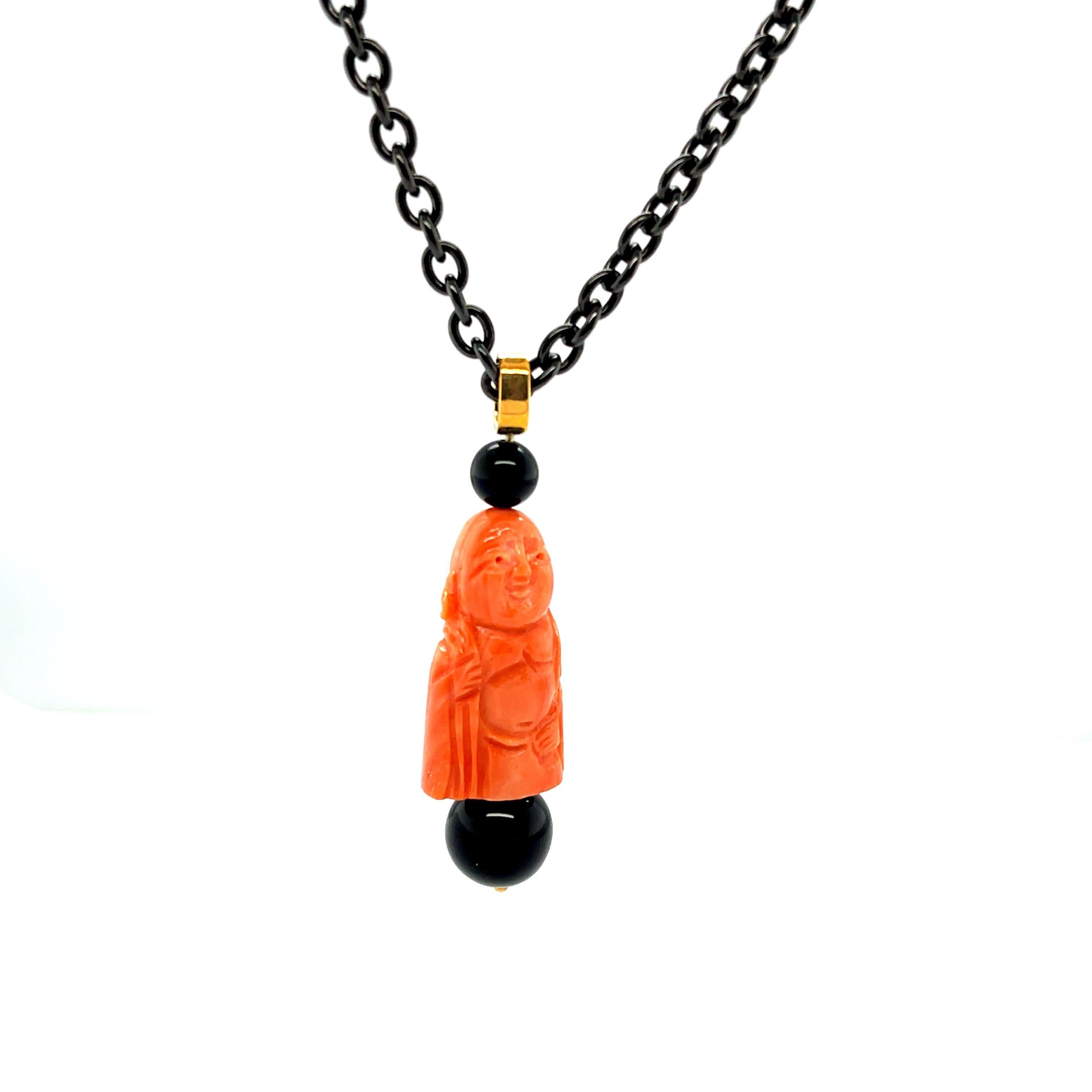 This unusual necklace is made of blackened steel and features Mediterranean coral that has been hand carved into a happy Buddhist deity. Accented with 2 shiny black onyx beads and an 18k yellow gold bail, this necklace is a unique combination