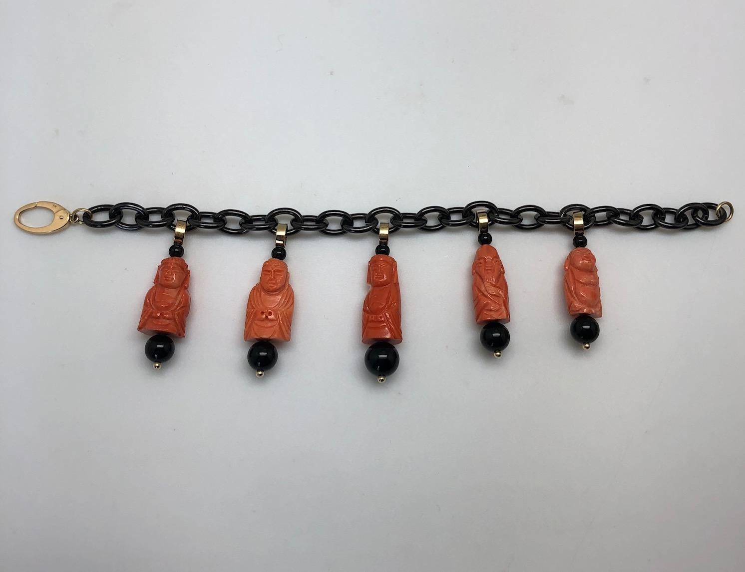 This fun charm bracelet is made of blackened stainless steel links and features 5 Mediterranean coral charms that have been hand carved into happy Buddhas and deities. Set with onyx beads, 18k yellow gold accents and an 18k yellow gold clasp, this