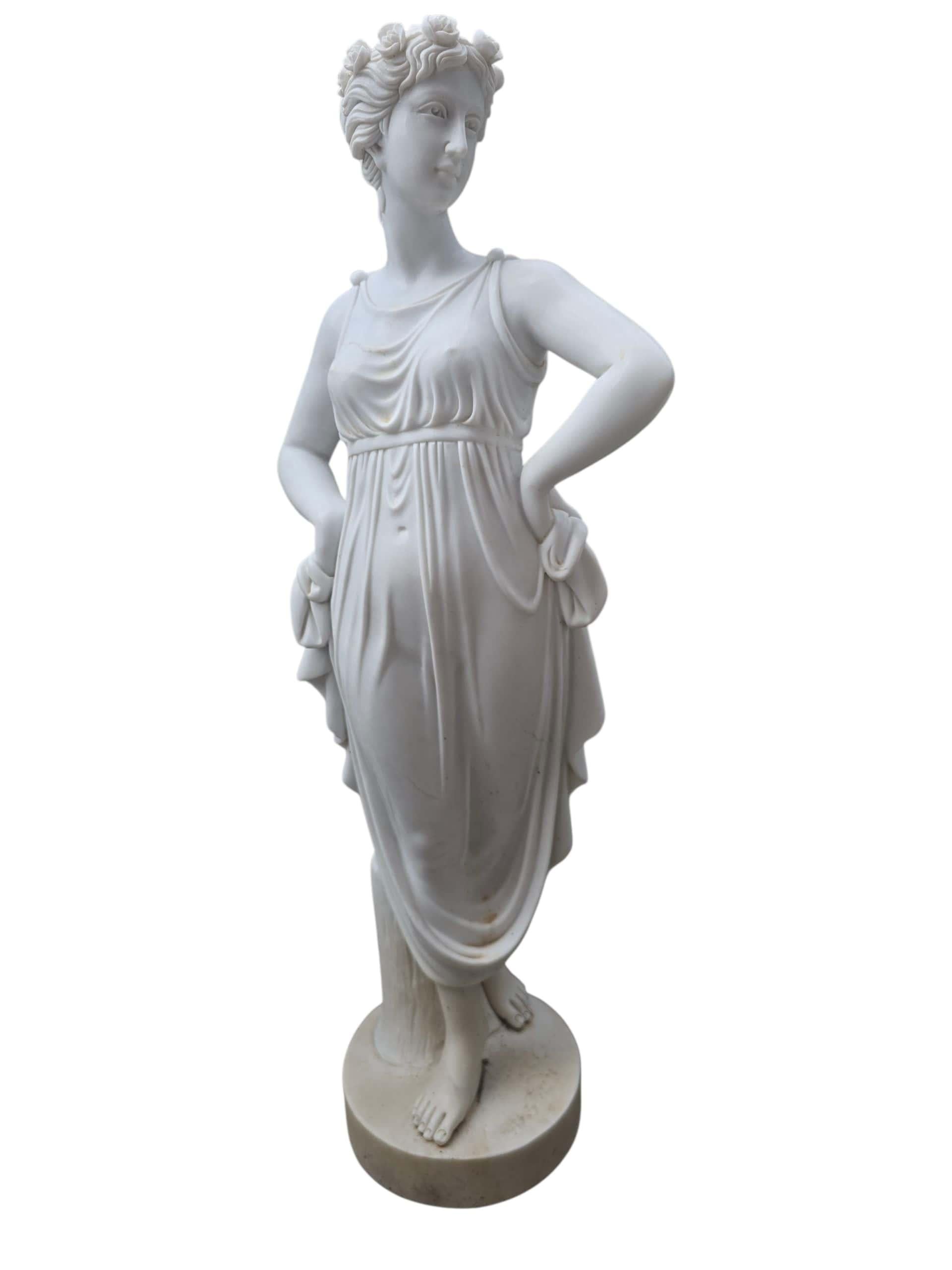 Elegante escultura de mármol tallada a mano, realizada en Italia durante el siglo XX, que representa a una elegante joven con un atuendo del siglo XIX. Ejecutada en fino mármol blanco italiano, la figura se representa con expresión serena y ropajes