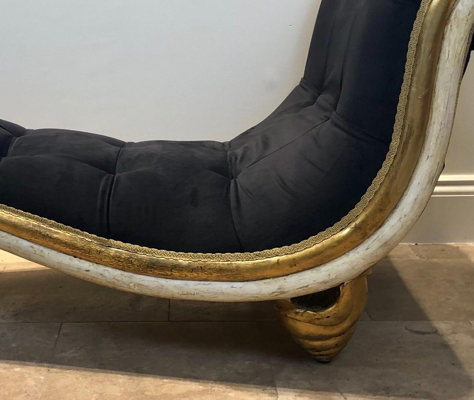 An extraordinary and unique chaise lounge all hand carved with distressed gilding and paintwork. This piece has been newly upholstered in buttoned black velvet, is curved at both ends and sits on gilded seashell shaped feet. This is an exceptional