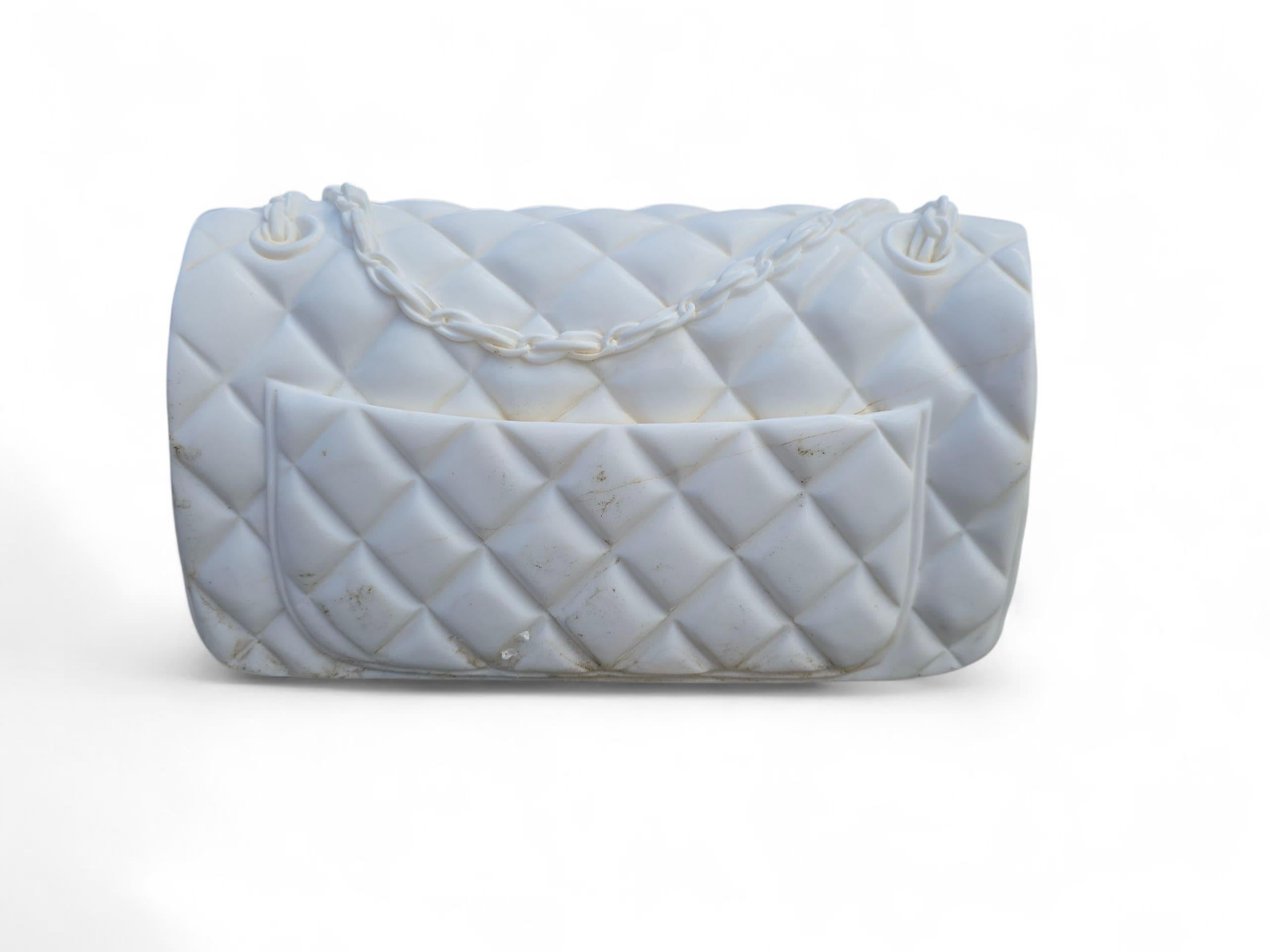 Einzigartige und dekorative Skulptur der ikonischen Chanel-Handtasche, sorgfältig von Hand aus feinem weißen italienischen Marmor geschnitzt. Dieses kunstvolle Stück ist eine Nachbildung der Eleganz und der Details des klassischen Steppdesigns,