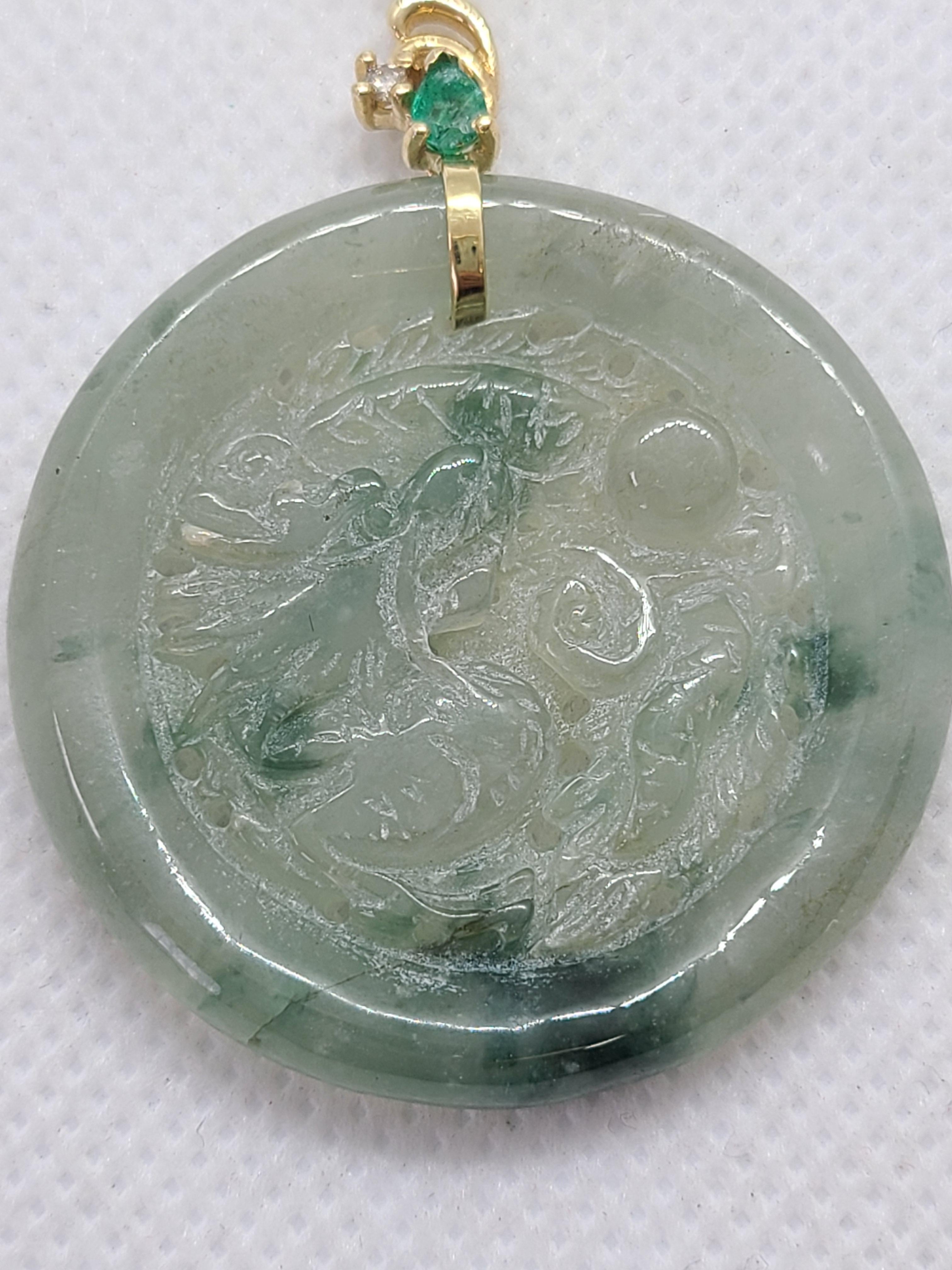 Featuring a hand-carved natural jade dragon guarding a pearl—symbol of good luck, wisdom, peace, and auspicious energy—this pendant is accented with emerald and diamond. Set in a 14K yellow gold mounting, the jade centerpiece measures approximately