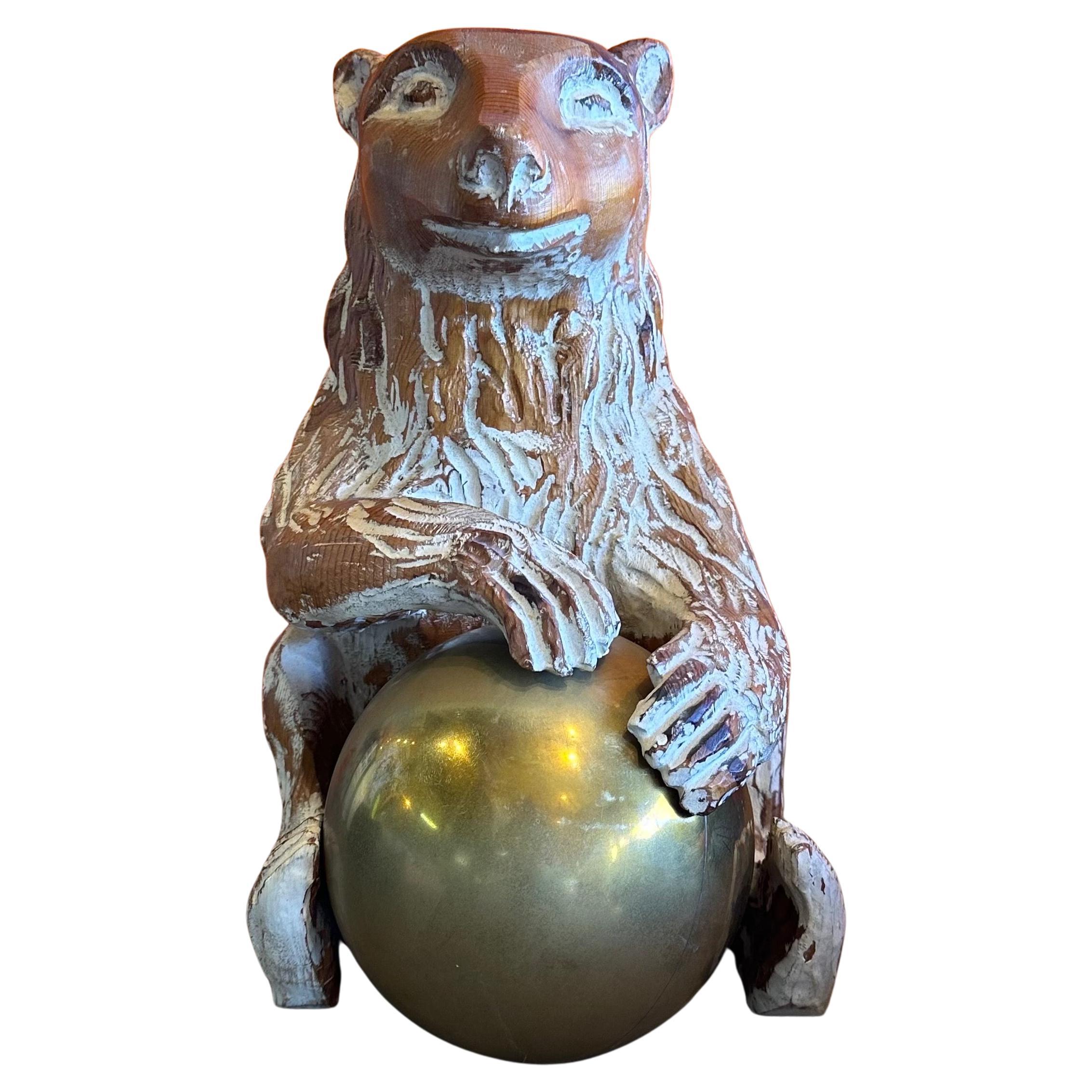 A nice hand carved knotty pine wood and brass bear sculpture by Sarreid, circa 1970s. The sculpture, which was made in Spain, is in very good condition and has a white wash overlay finish.  The bear is playing with a brass ball.   The piece measures