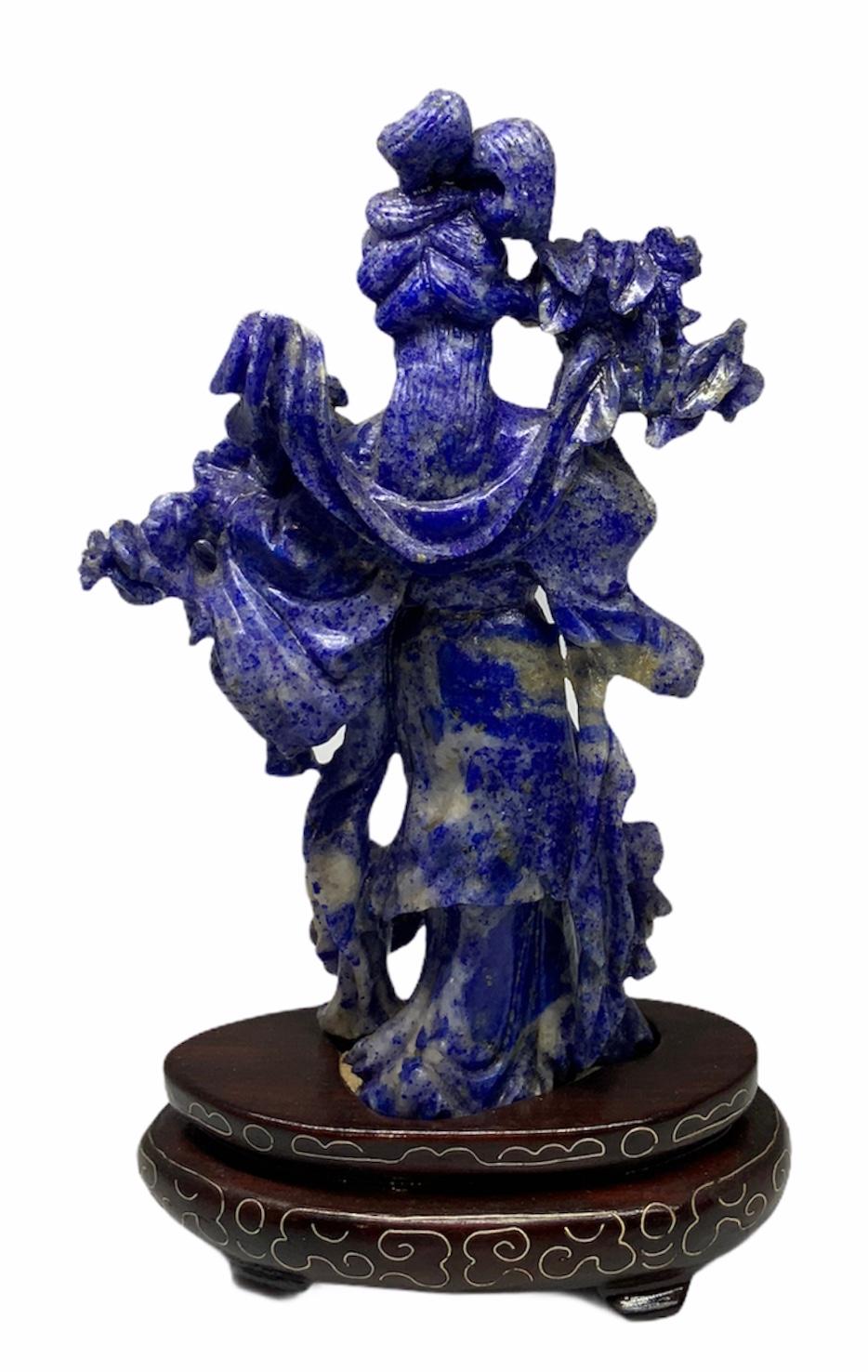 Finely hand carved lapis lazuli small sculpture of He Xiangu with a typical Chinese heavy long wavy dress and a kind of Chinese hair arrangement. She is holding a bunch of lotus flowers in her right hand and a basket of them in her left hand. The