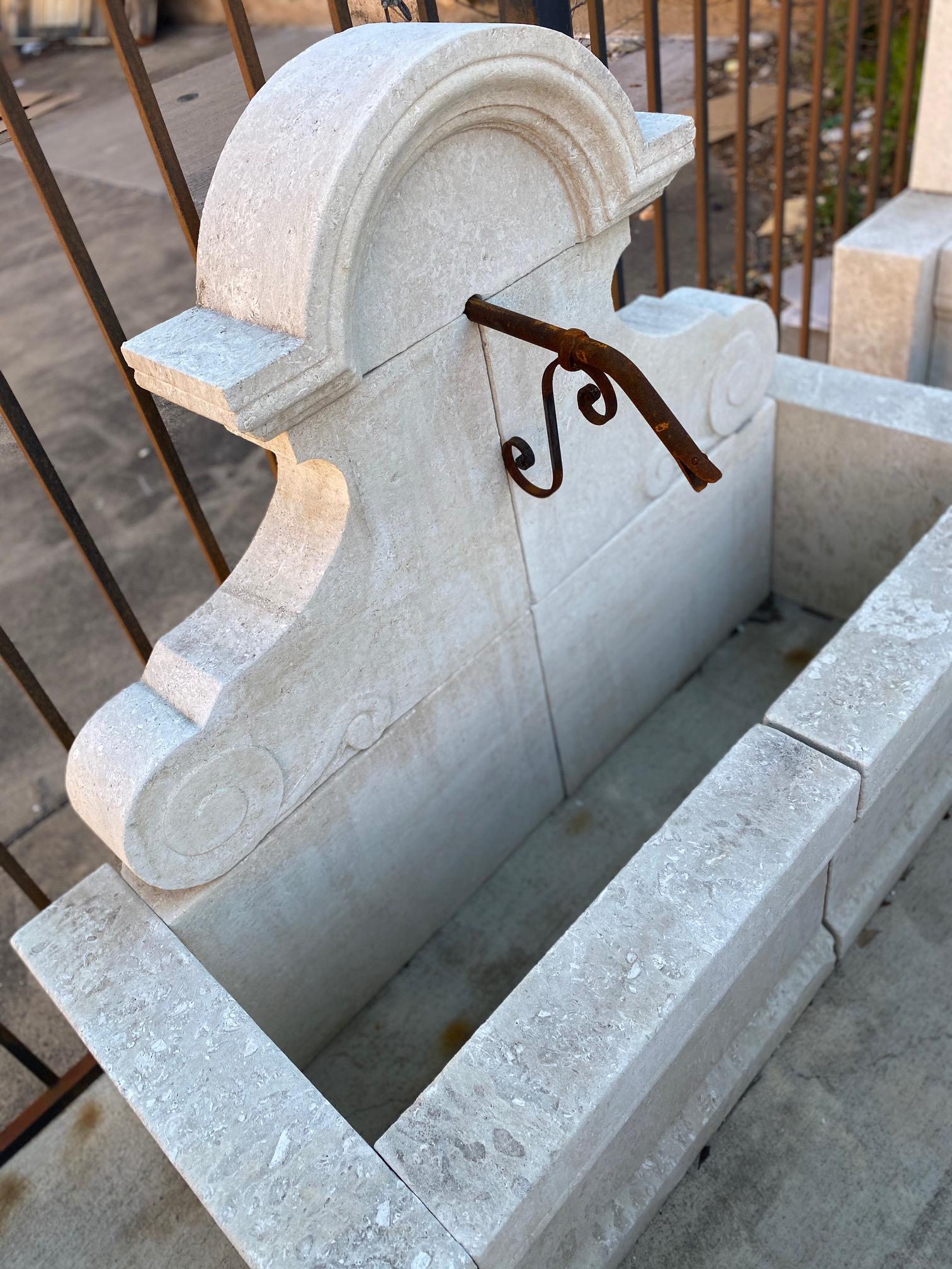Here we offer a hand-carved limestone wall fountain with an iron down spout. This fountain has a classical French bonnet design for the crown and detail carvings at the base of the backplate that complete the French feel of the piece. Let the