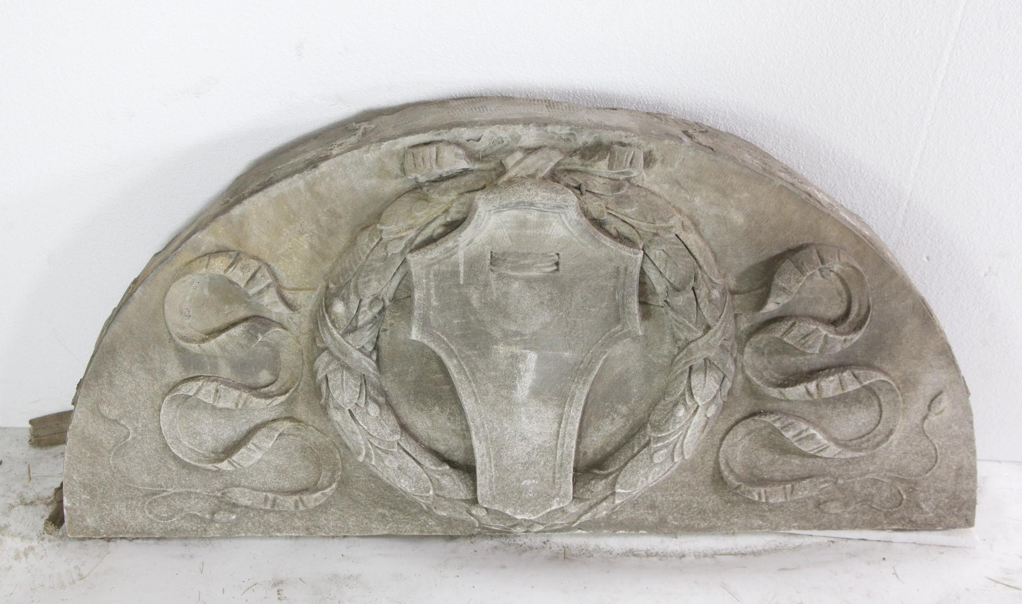 Late 19th century arched limestone transom pediment featuring a hand carved center shield and wreath, with ribbons fluttering out breezily on each side. This can be seen at our 400 Gilligan St location in Scranton, PA.