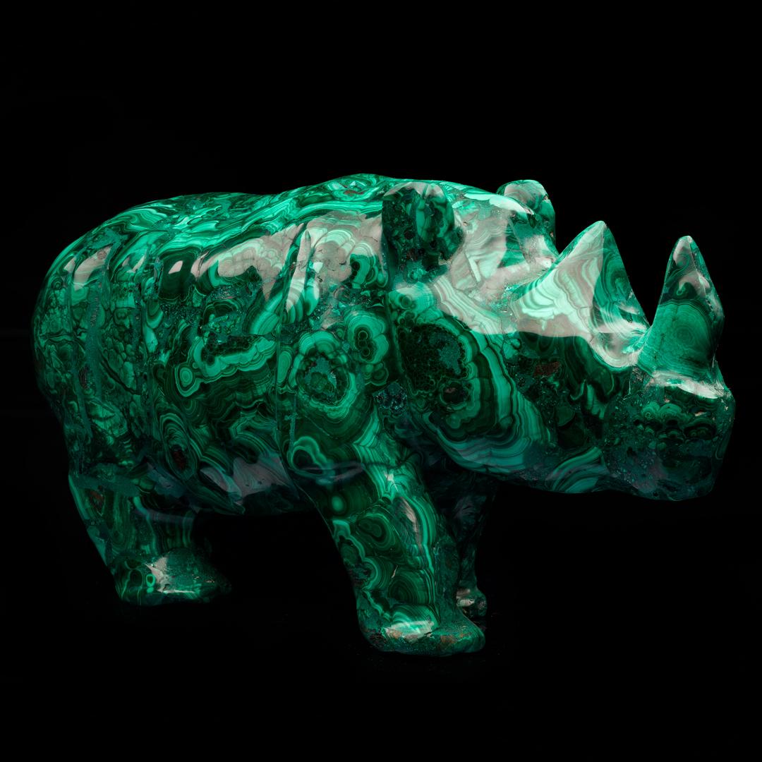 This luscious green copper carbonate mineral specimen from the DRC has been expertly hand-carved into a substantially sized 10 pound rhinoceros and hand-polished to a brilliant luster to enhance its gorgeous colors and banding. Malachite was