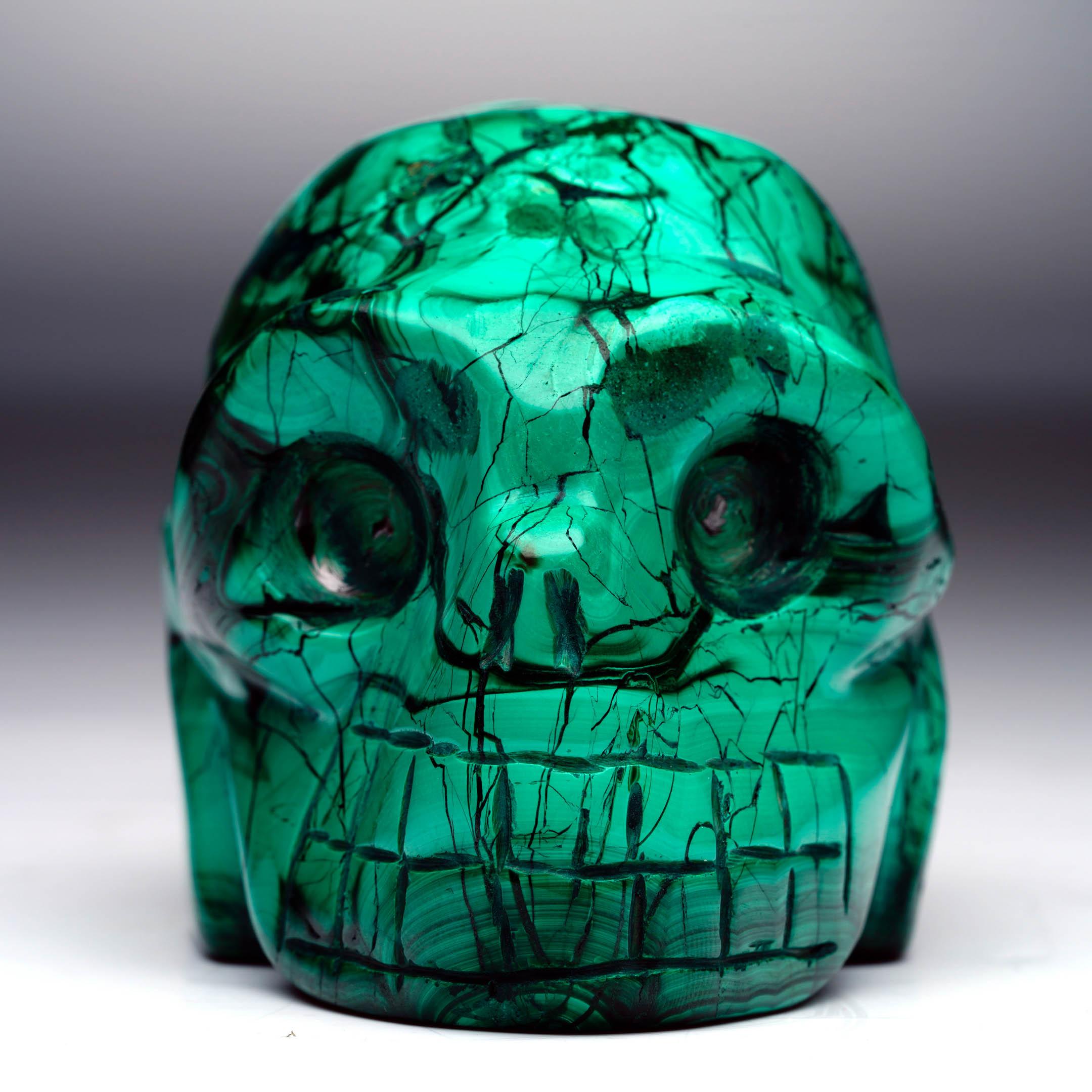 Questo teschio di malachite intagliato a mano cattura la bellezza tipica del minerale in una raffinata forma decorativa. Stupefacenti bande di smeraldo intenso e verde più chiaro creano drammatici anelli concentrici, vortici fluenti e audaci motivi