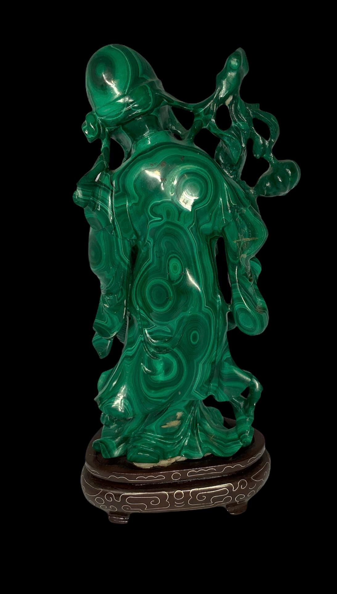Hand carved Malachite of small sculpture of Shou Xing Gong depicting a happy face old man with beard and a heavy oriental robe. He is holding in his right hand a staff with branches of peaches twisting around it and in the left hand a basket full of