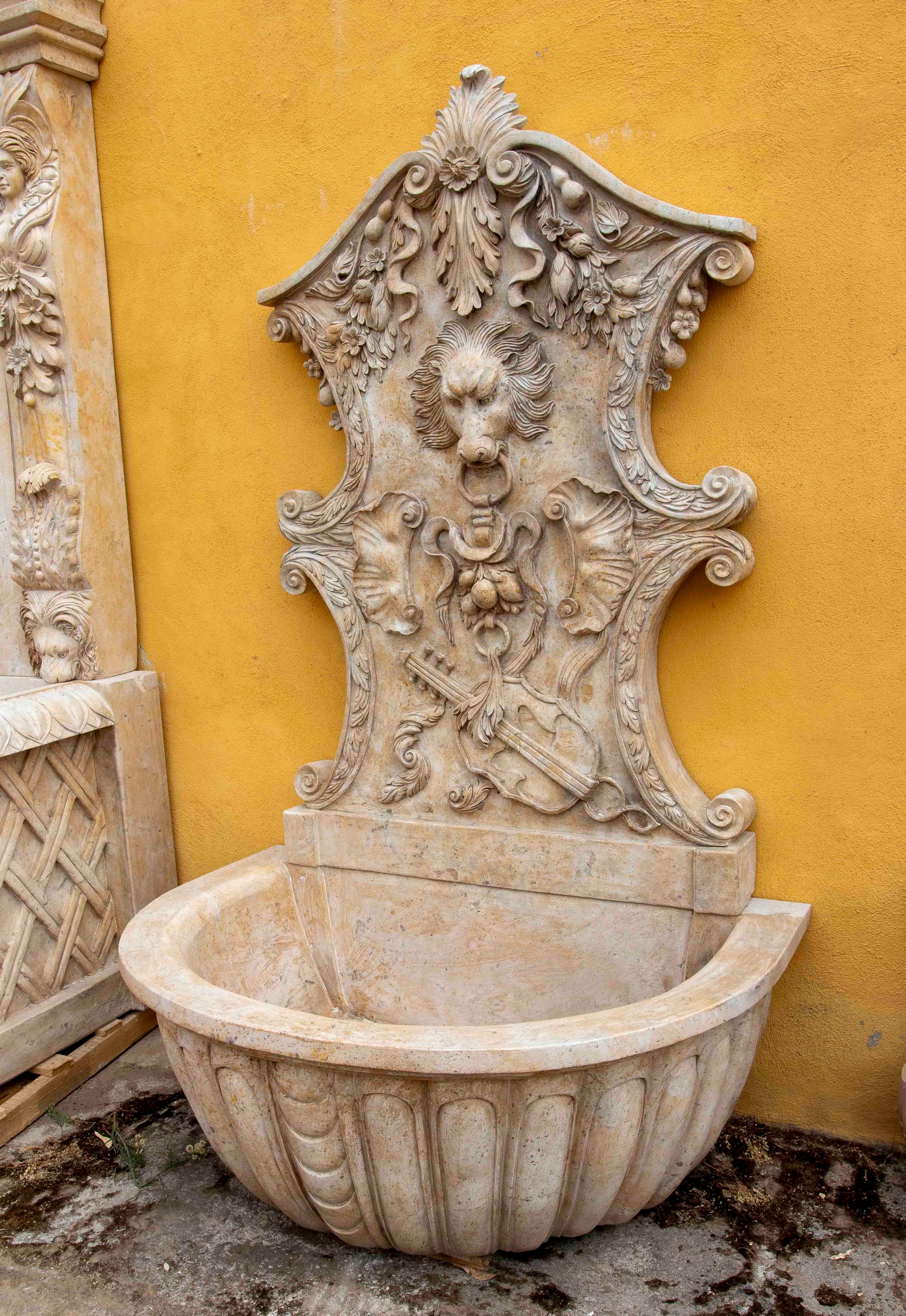 Imponente fuente mural de mármol tallado de inspiración barroca, decorada con motivos florales y una majestuosa máscara de león como fuente central. La pieza cuenta con una pila semicircular profunda, ideal tanto para uso interior como exterior. Su