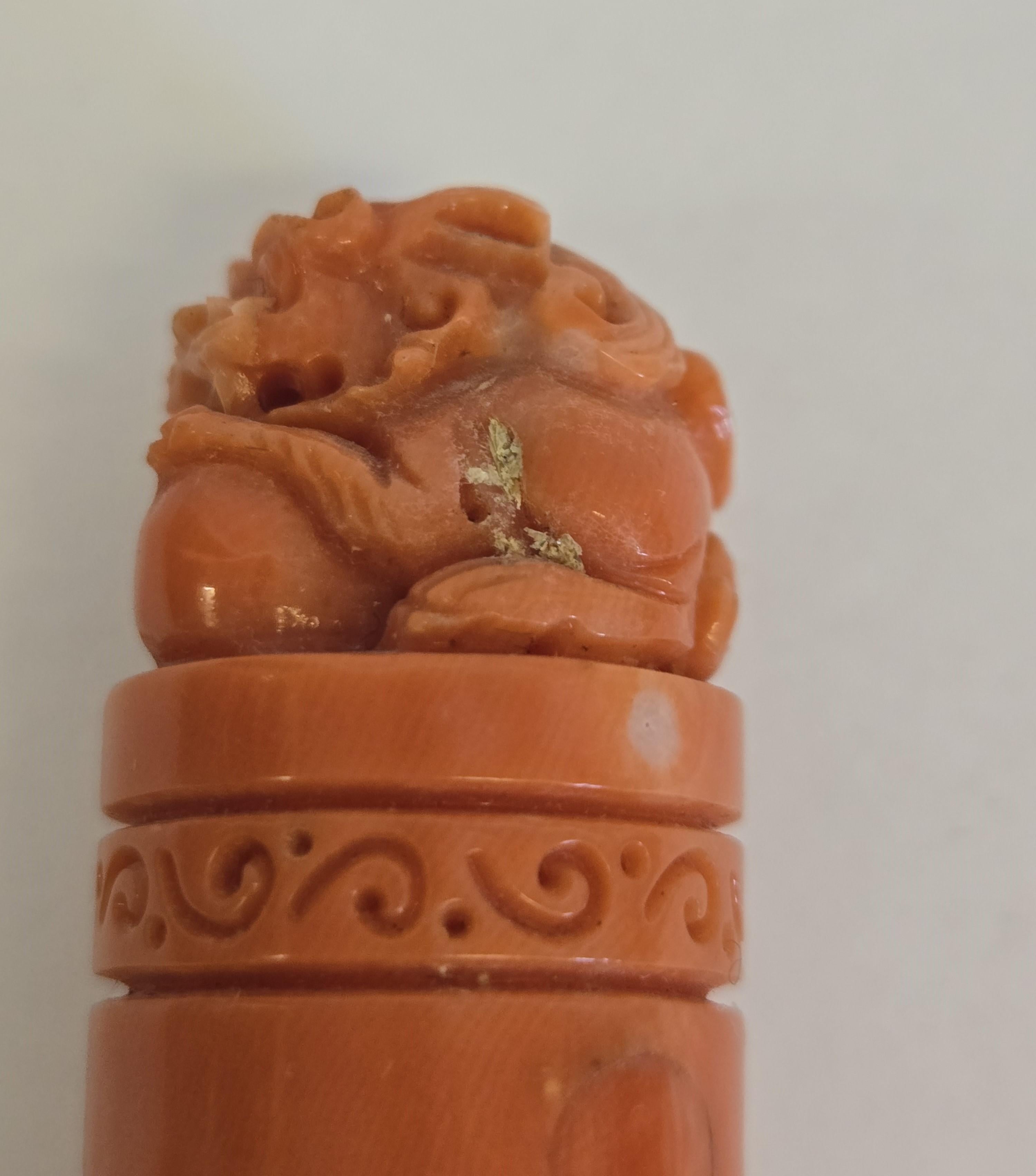 Ce timbre en corail rouge orange naturel est sculpté à la main et représente un lion chinois paisible jouant avec un ballon, symbole traditionnel de joie, de protection et d'harmonie. La sculpture présente des têtes de lion finement détaillées avec