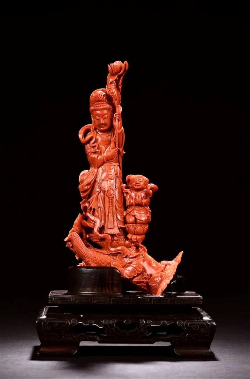 Cette sculpture en corail rouge orange naturel, sculptée à la main, représente un enfant de la foire vénérant Guanyin, la déesse bouddhiste de la miséricorde et de la compassion. Guanyin se tient sur une couronne de lotus au-dessus des nuages,