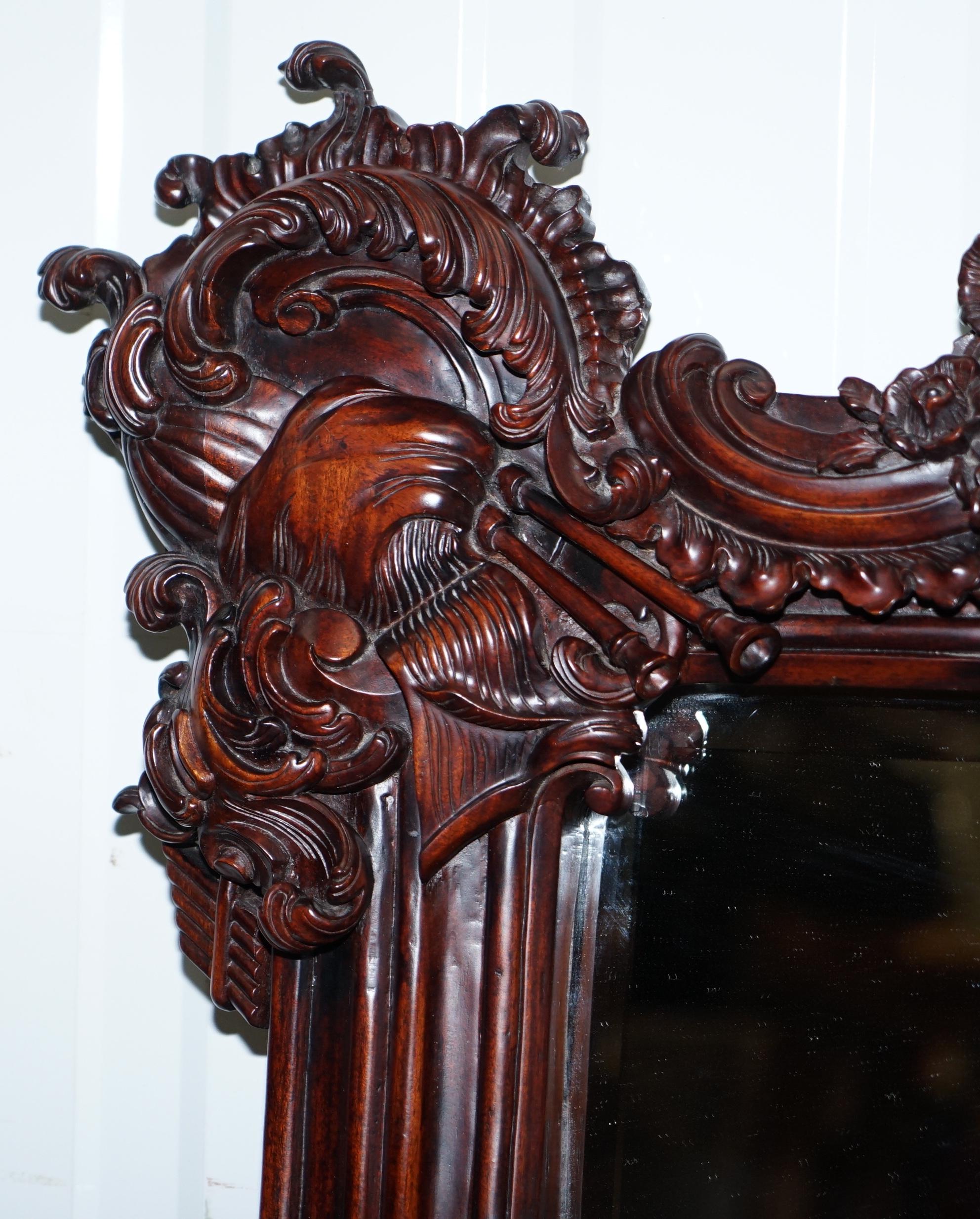 We are delighted to offer for sale this extremely ornate hand carved from solid Mahogany wall mirror

There is a lot going on with this mirror, at the top left you have musical pipes, the middle an armorial crest surrounded by flowers, top right a