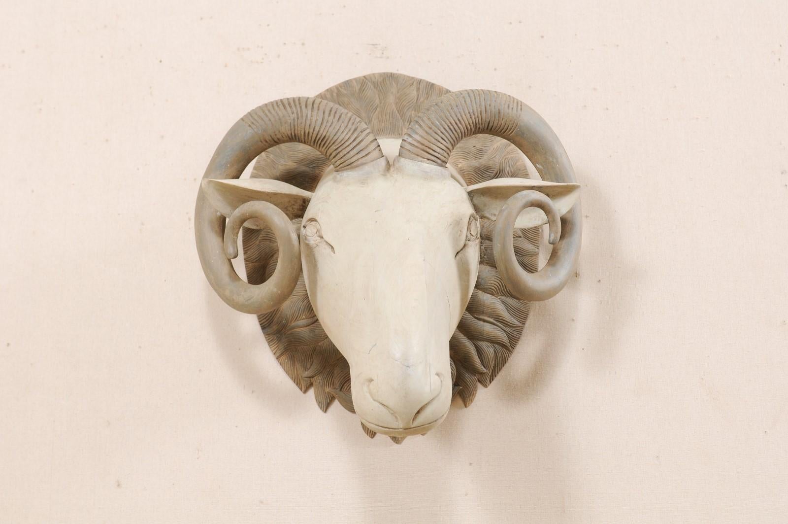 A handsome hand carved wooden ram's head wall ornament. This artisan created wooden ram's head features a hand carved, forward facing three-dimensional ram face with beautifully curled and textured horns, mounted onto a rounded wooden back plate